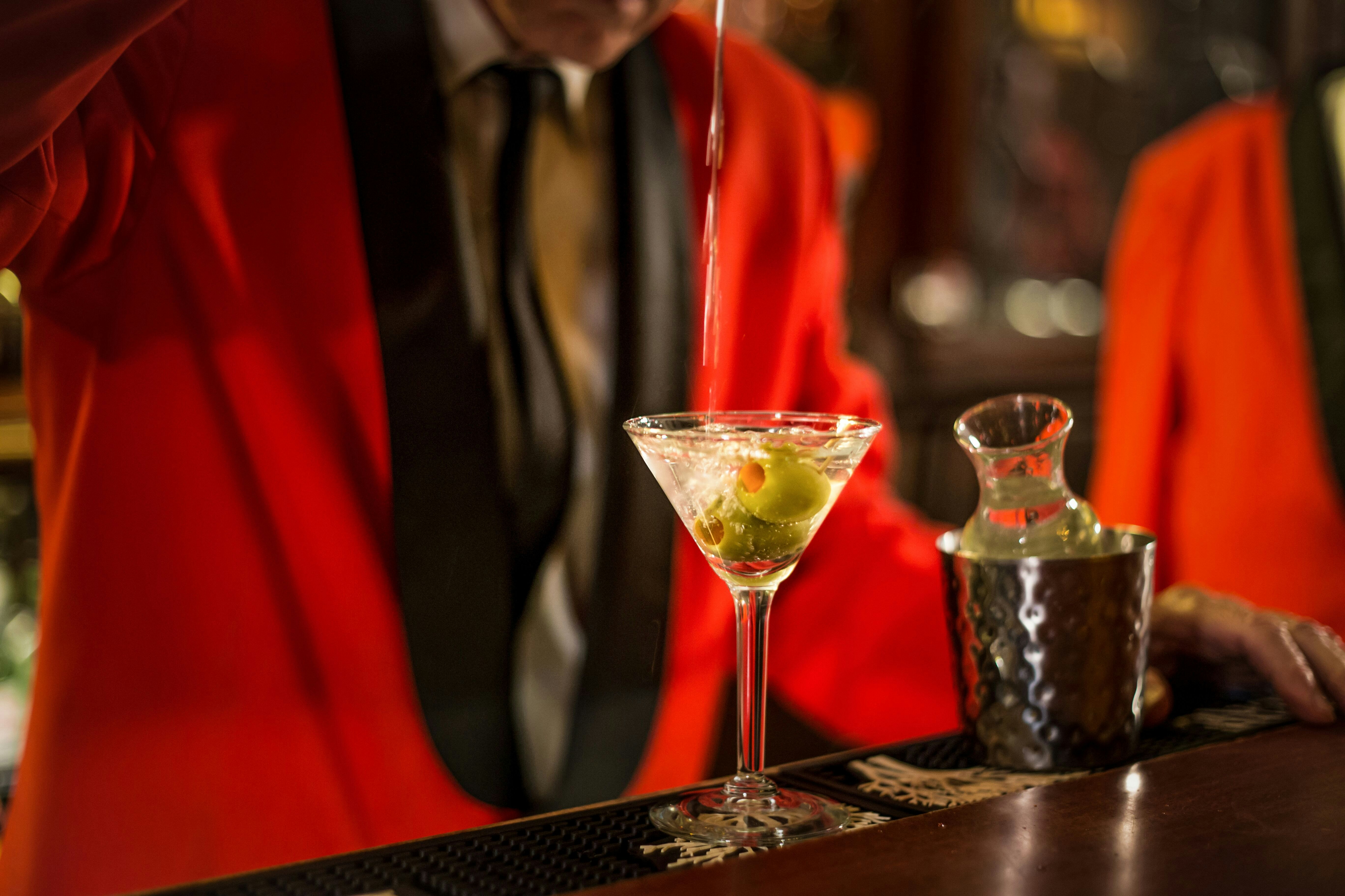 A martini is being poured with an olive in the glass. 