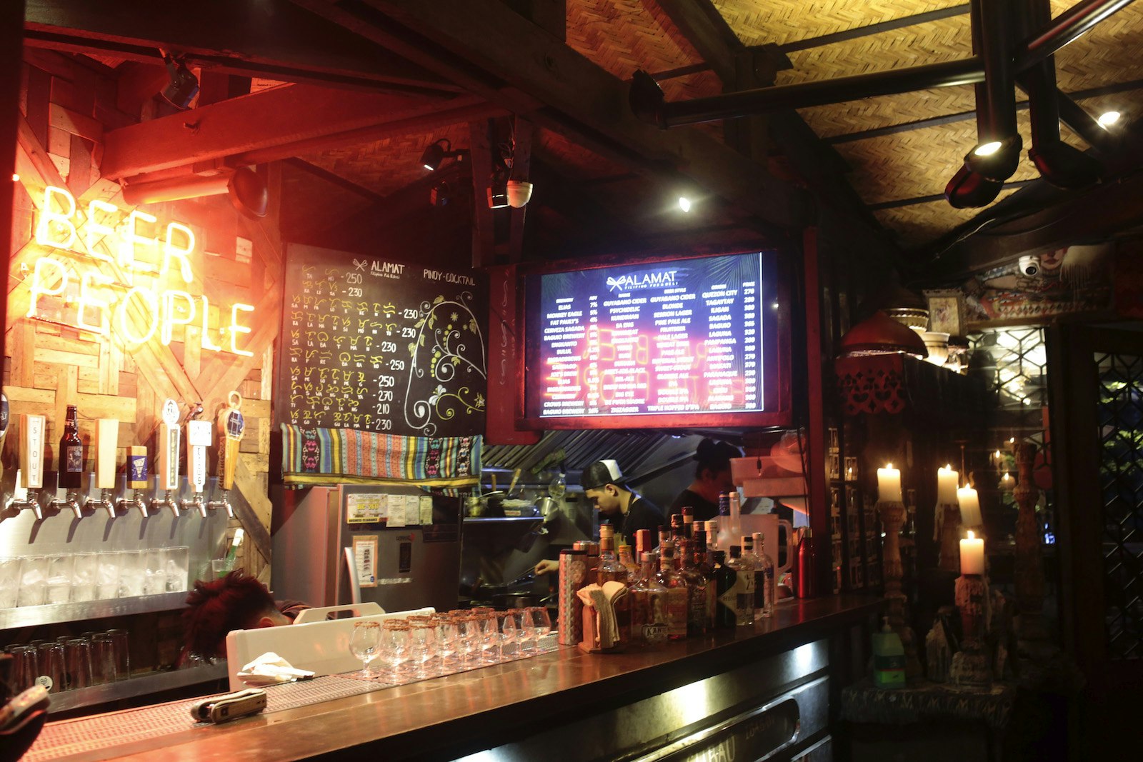 A bar with red lighting, candles in the corner and sign above the tap that reads, 'Beer People'