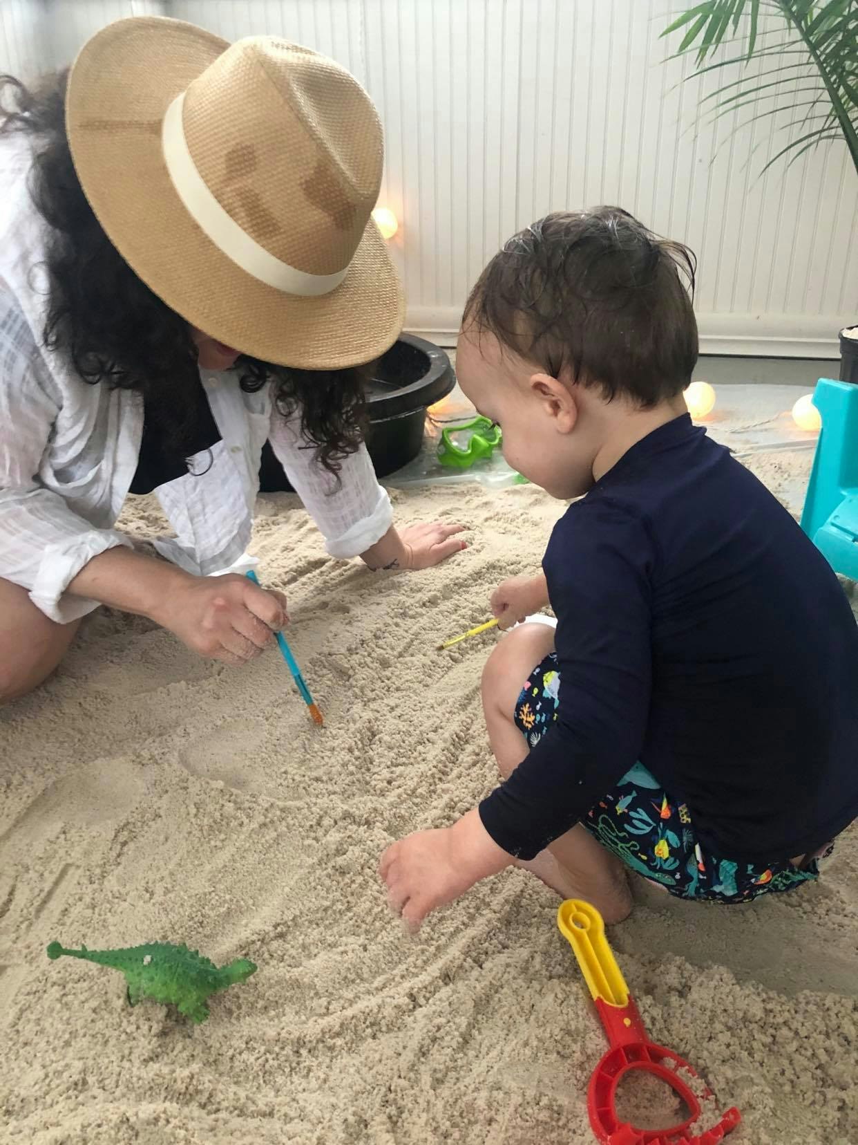 A woman plays with sand with her son indoors. 
