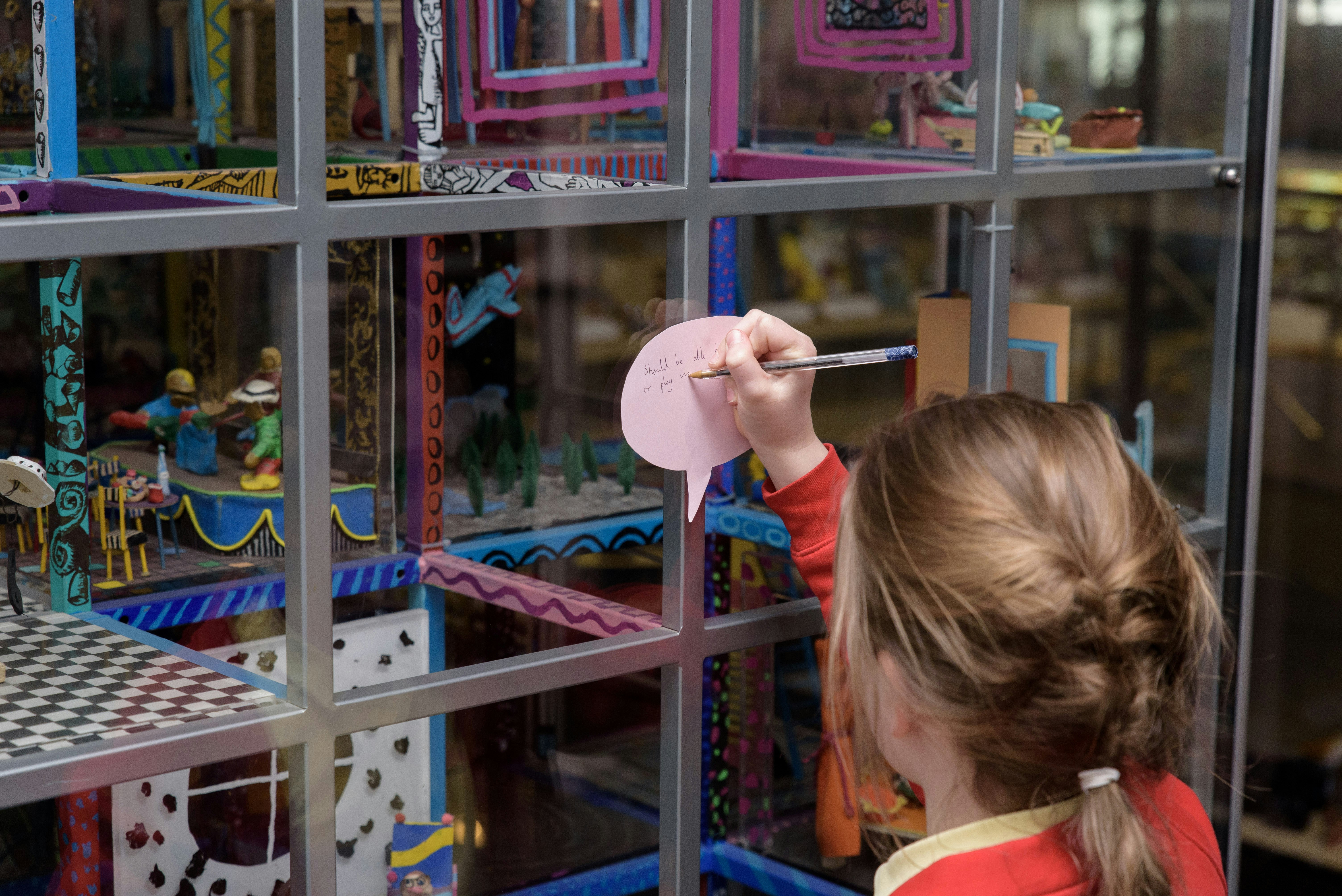 A young girl writes on a Post-it inside a museum