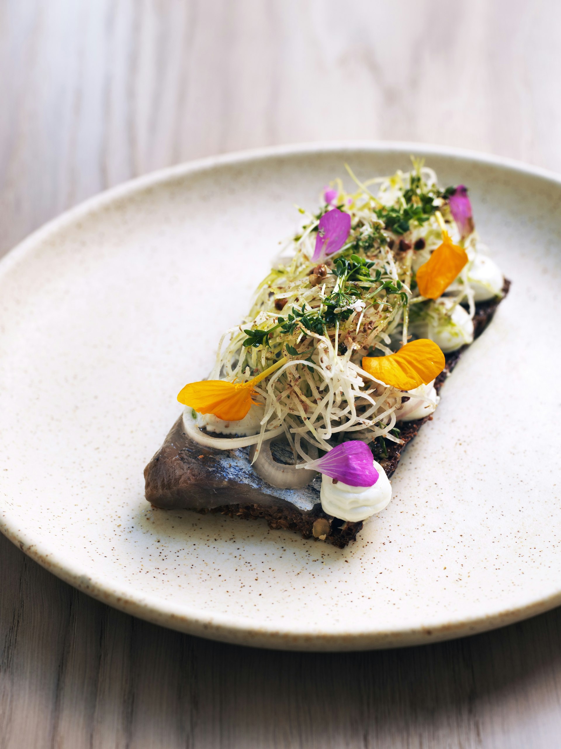 An open sandwich with herring, topped with orange and purple flowers