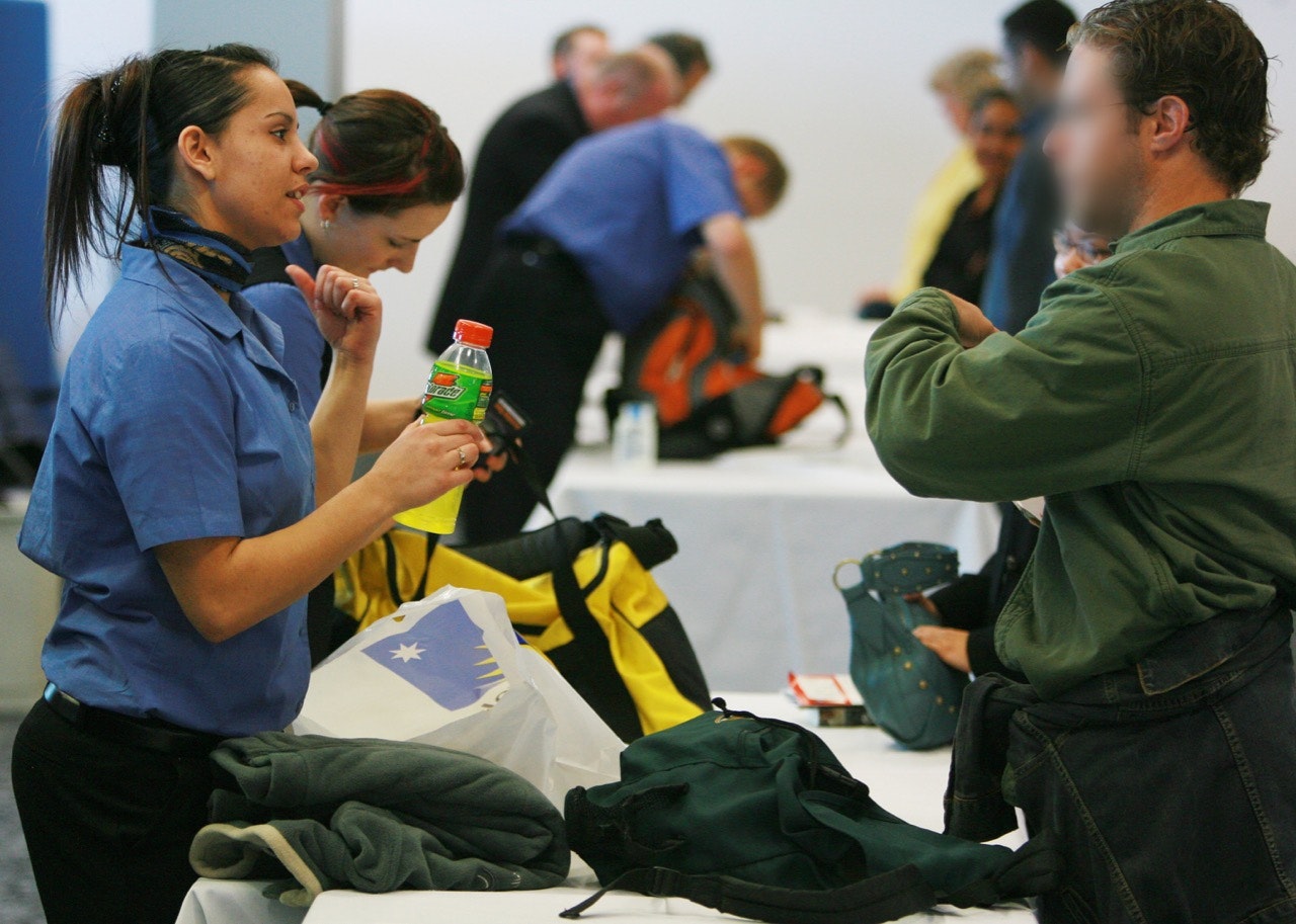 Security agent holding gatorade bottle talking to passenger