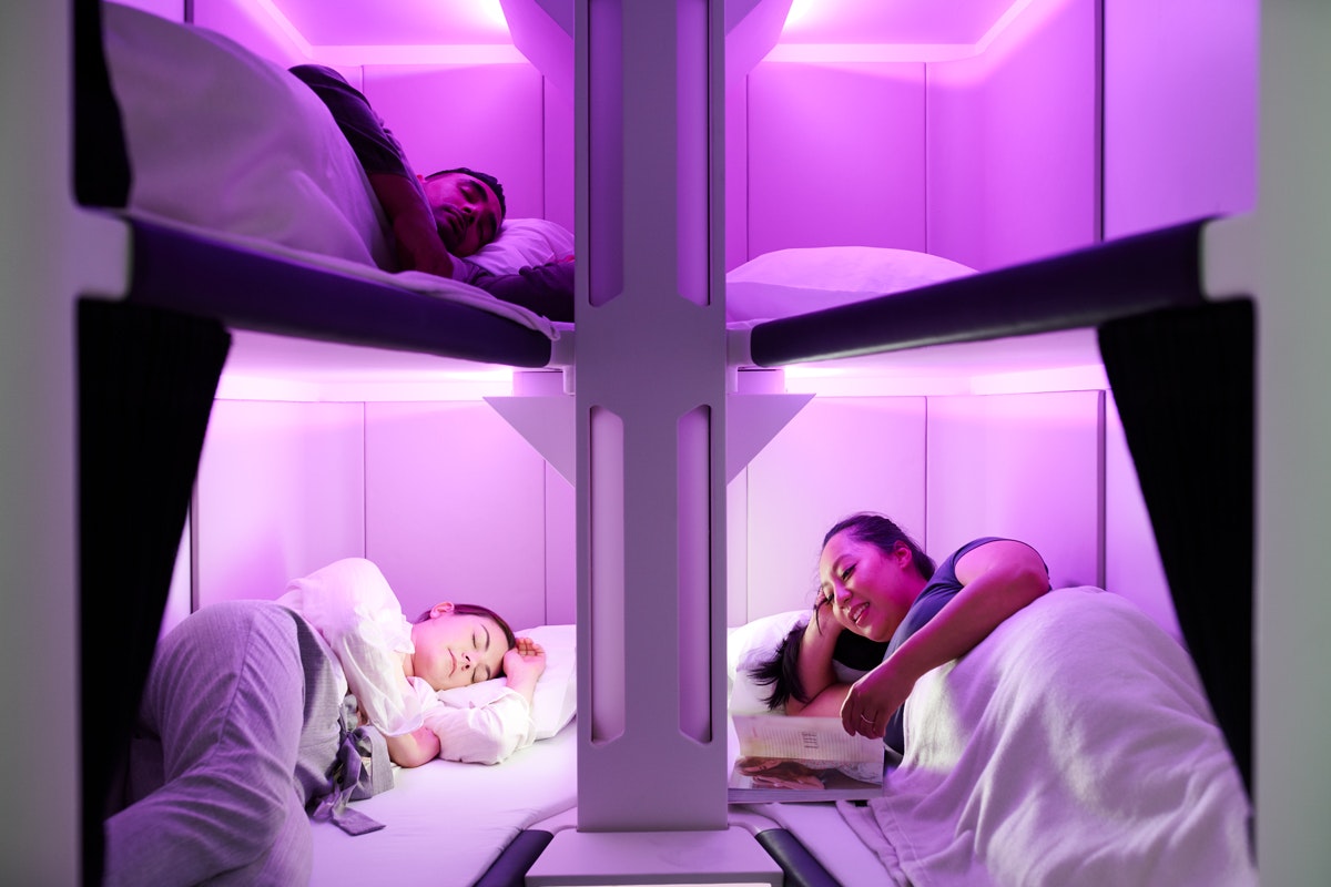People sleep in pod-style bunk beds in airplane cabin glowing with mood lighting
