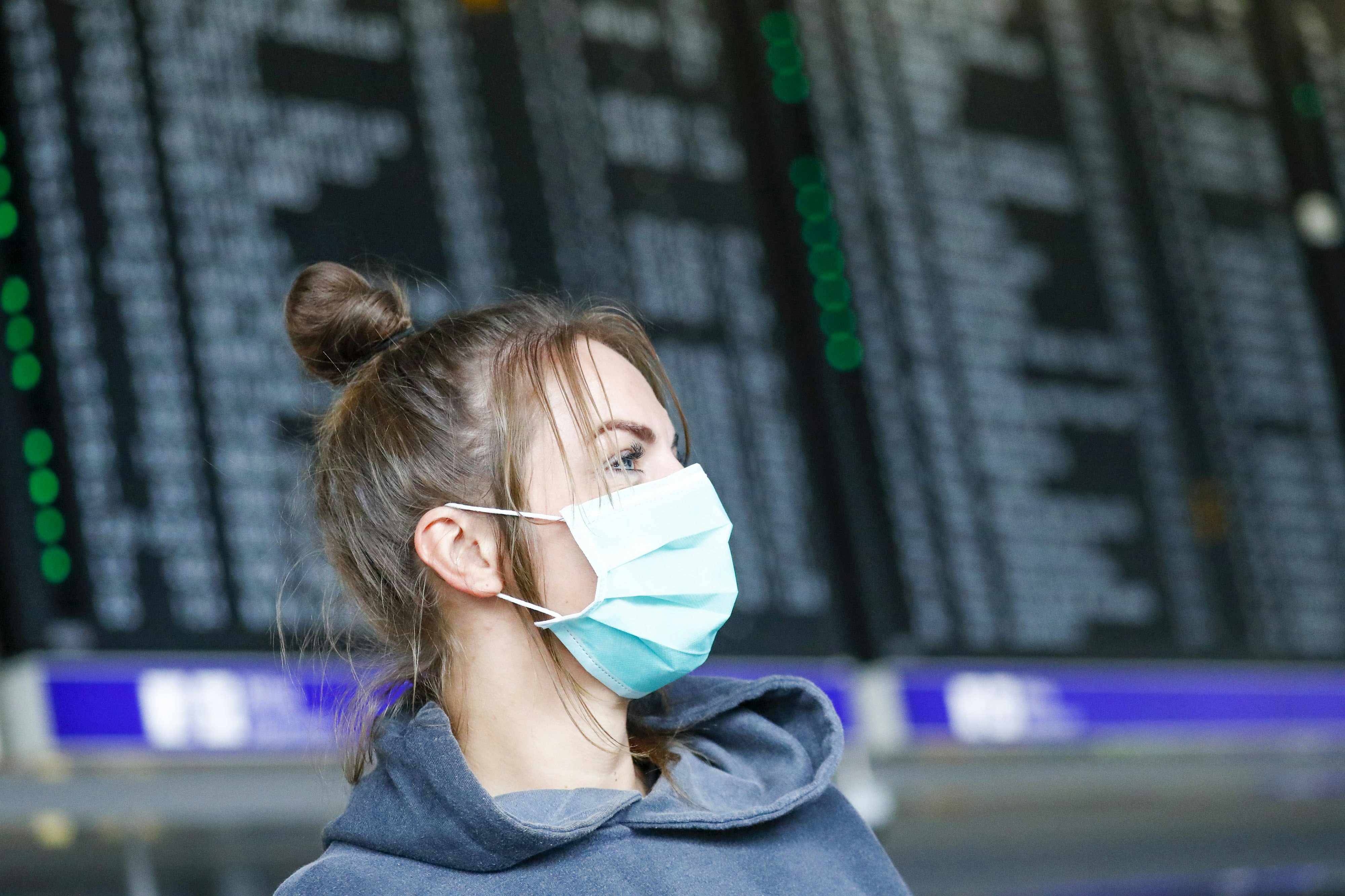 Female passenger wearing a face mask in front of an airport departures screen