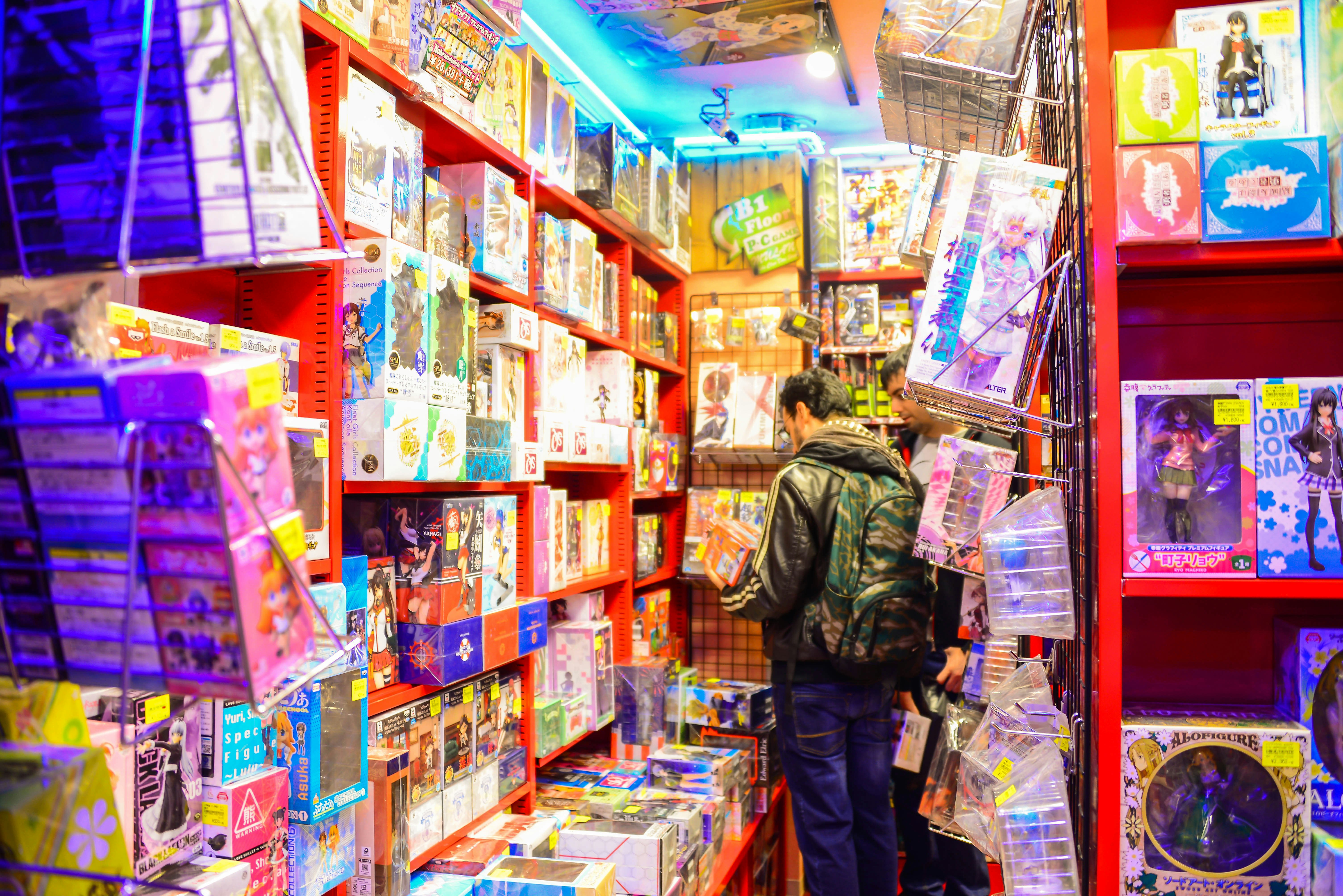 A man browses a comic book in a Manga store. The floor to ceiling walls around the shopper are filled with anime-style comics, toys and games.