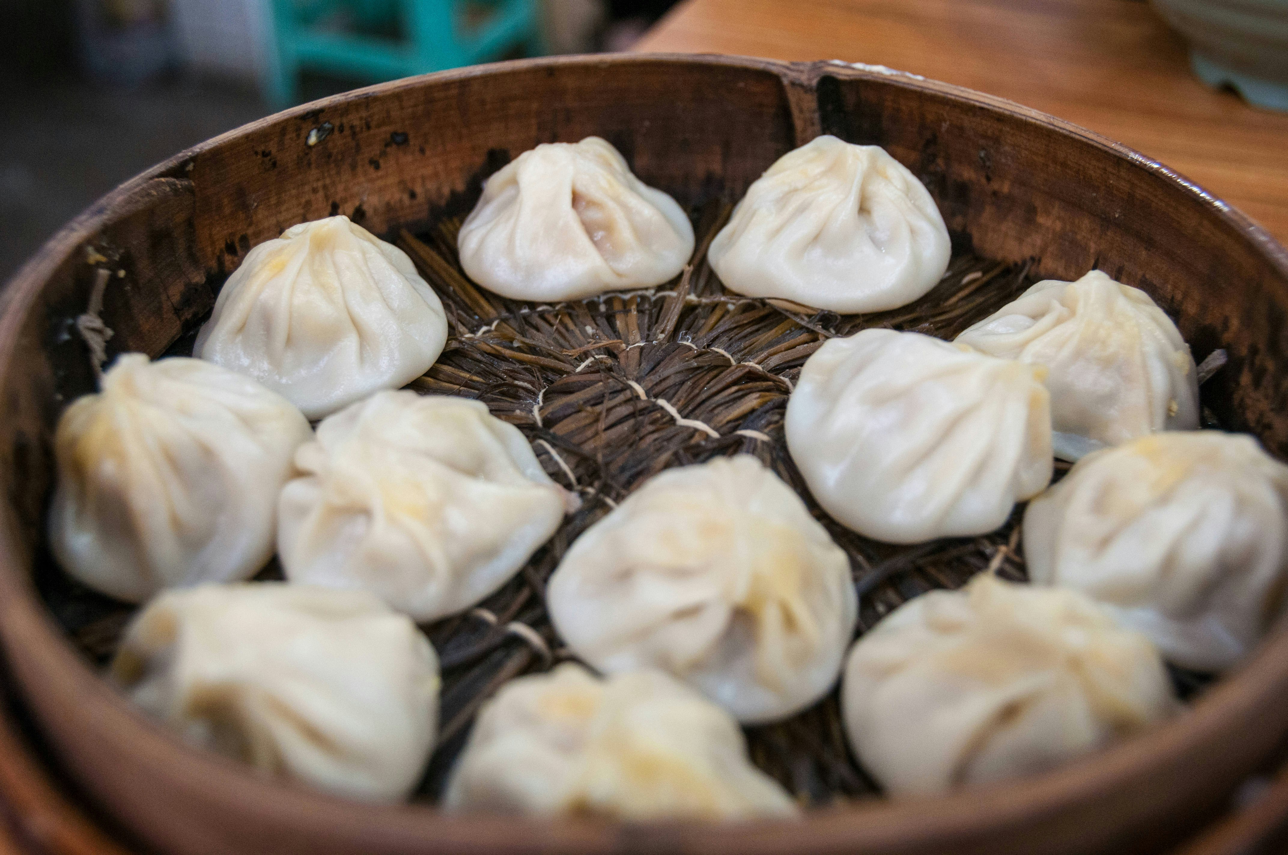 A number of white xiaolongbao (dumplings) cooling in a brown wicker basket on a tabletop.