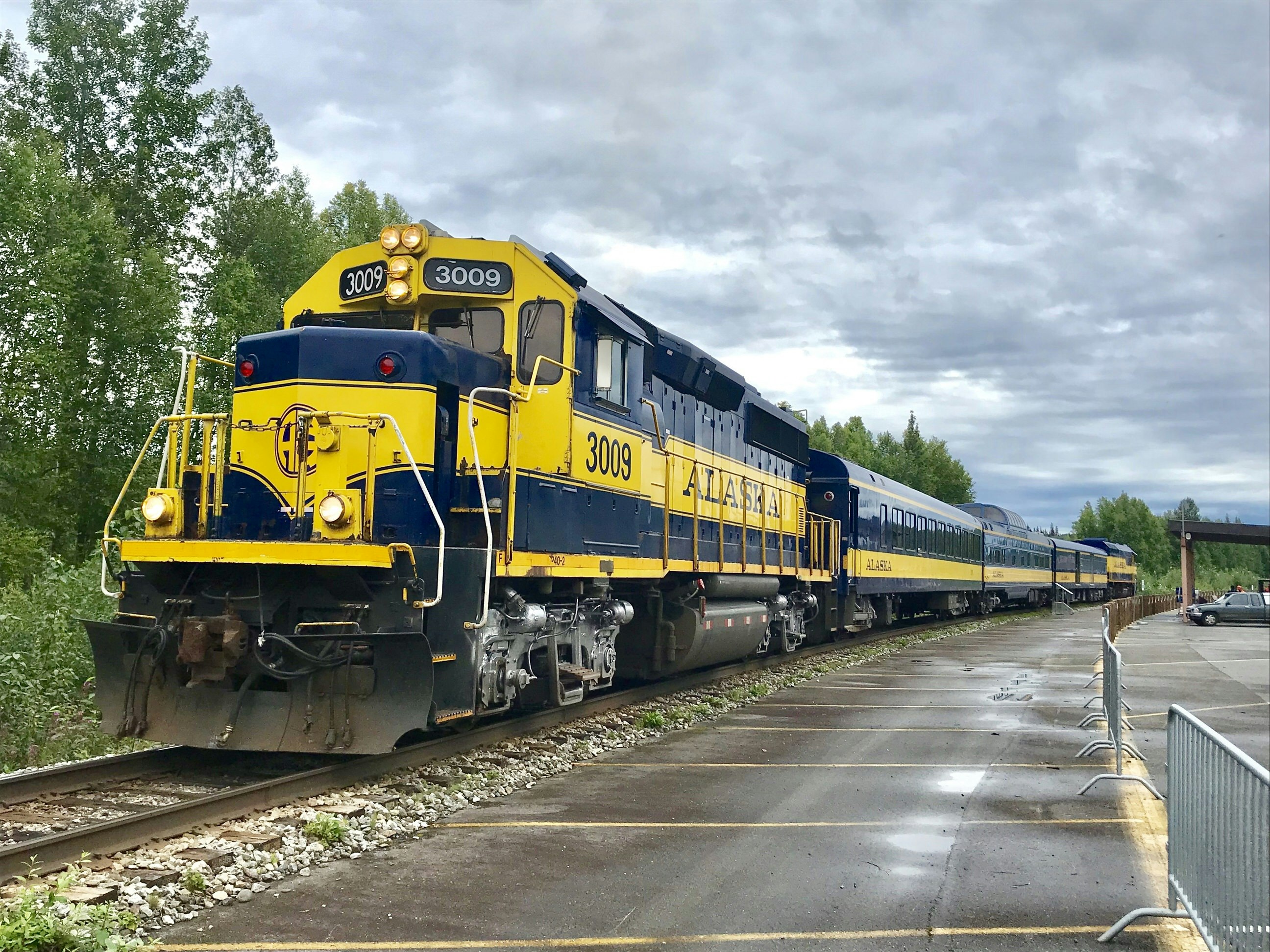 A sturdy navy and yellow train, standing on a platform. On the side of the front car, 'Alaska' is written in yellow letters