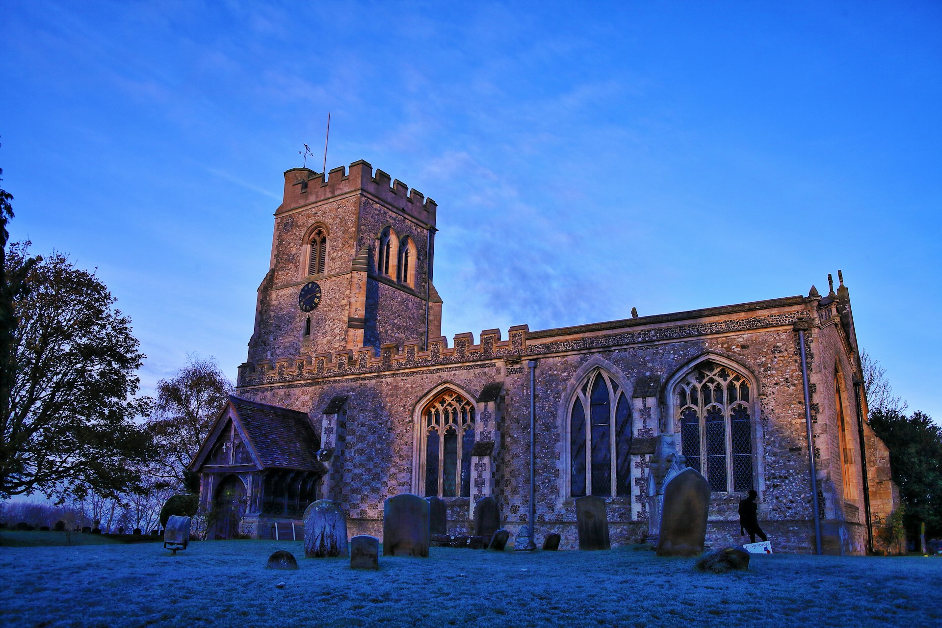 The outside of All Saints Church at dusk. A number of headstones are visible on the grass in front.