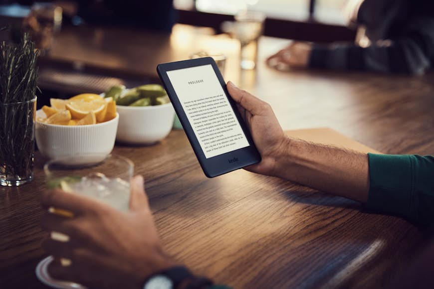 Mans händer som håller Kindle e-läsare på ett kafé