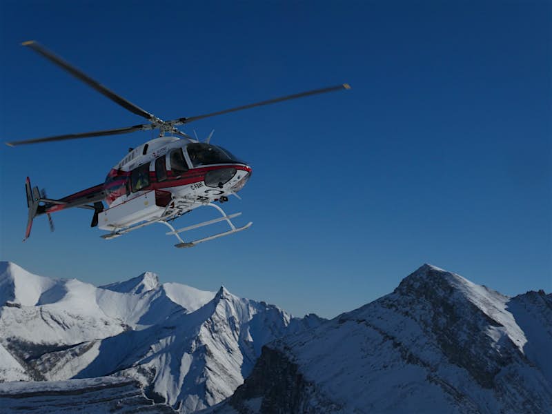 A helicopter hovers near snow capped mountains in winter at Banff and Lake Louise