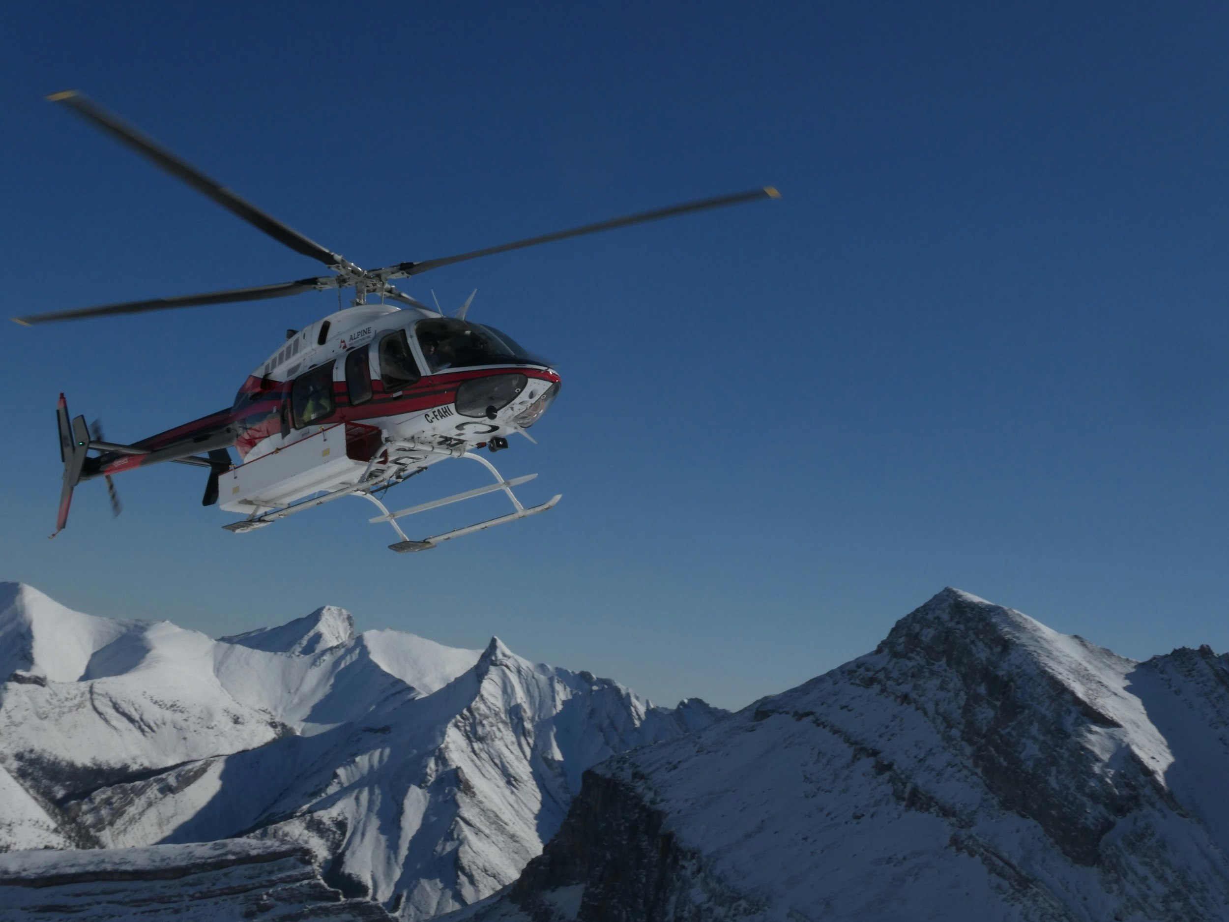 A helicopter hovers near snow capped mountains in winter at Banff and Lake Louise