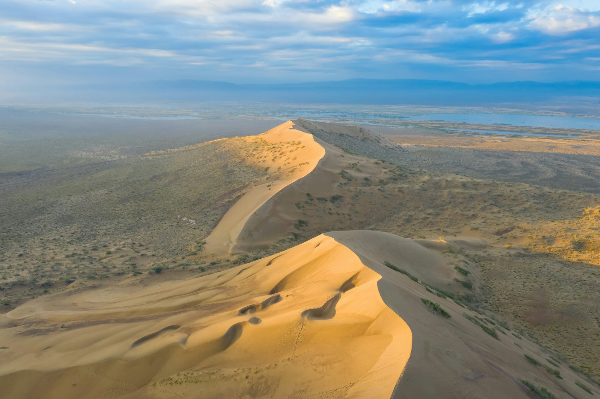 The Singing Sand Dune in Altyn-Emel National Park, Kazakhstan. The large sand dune is surrounded by a desert-like landscape on all sides.