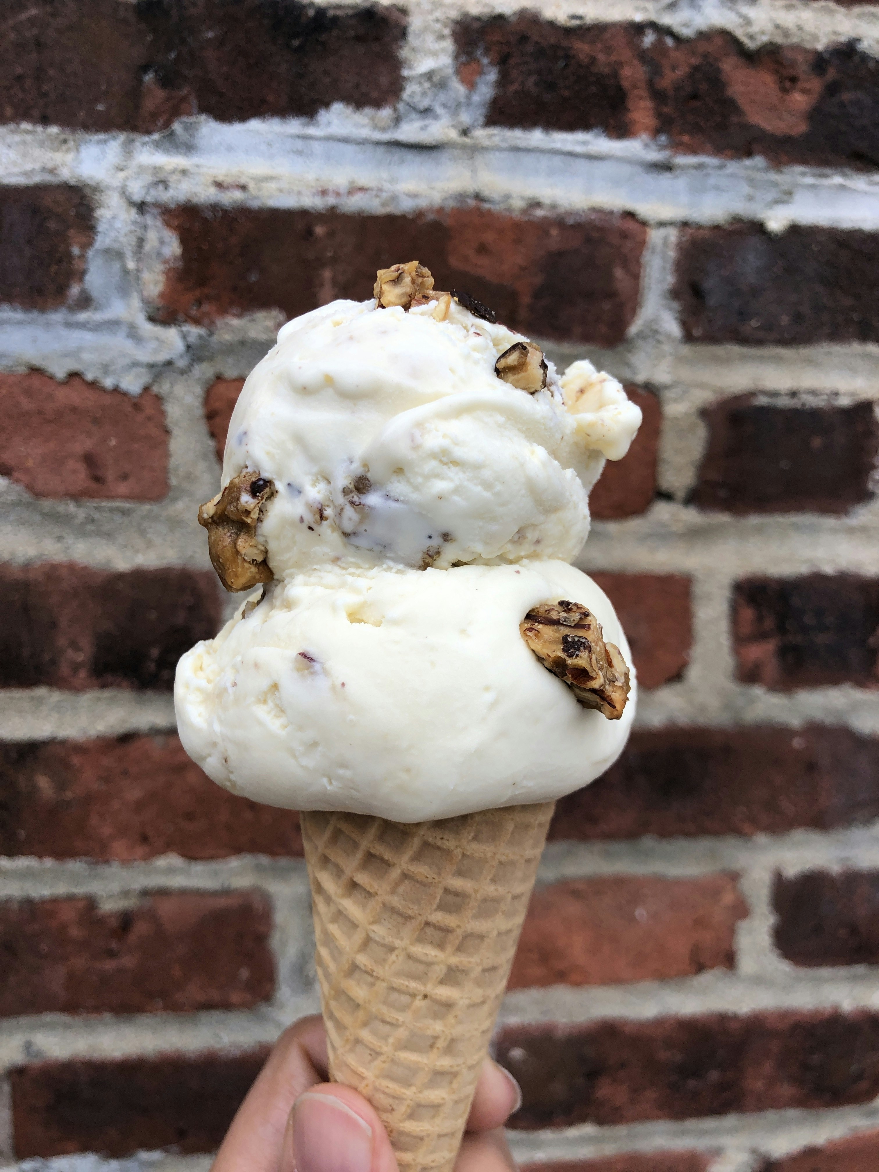 A two-scoop ice cream cone is held up against a brick background