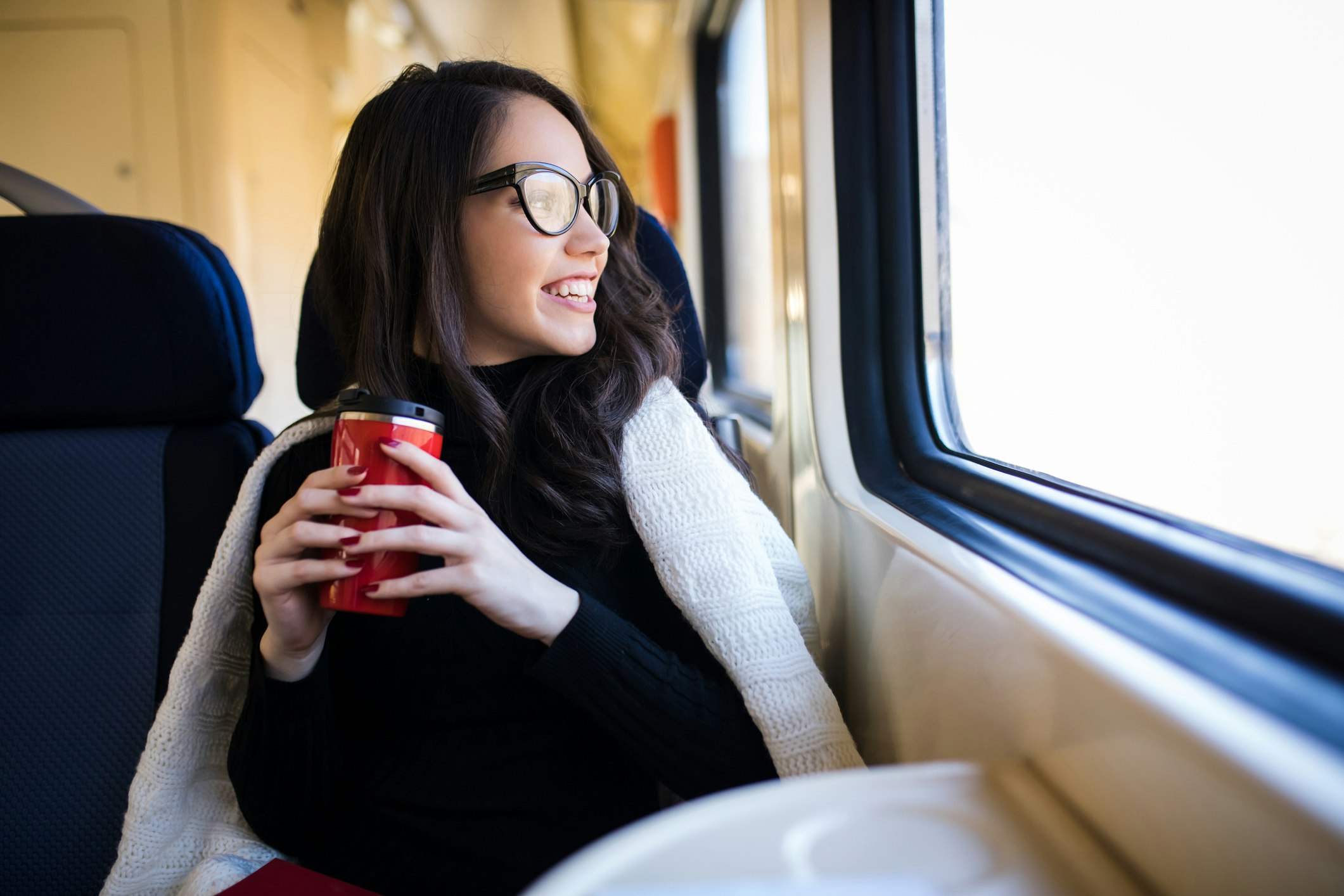 Young woman holding a coffee cup and looking out a train window