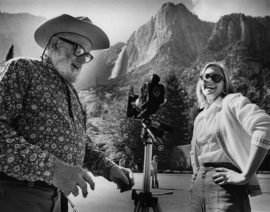 Ansel Adams skrattar med en kvinna när han tar ett foto av ett vattenfall;  hur man fotograferar Yosemite som Ansel Adams