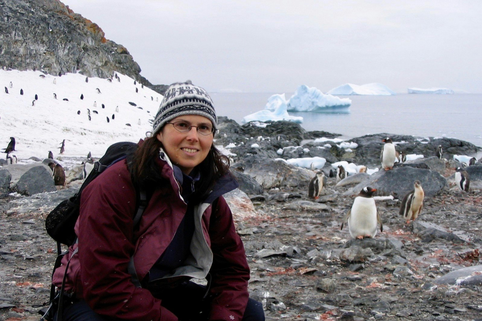 Marie-France poses next to some penguins near the coastline in Antarctica 