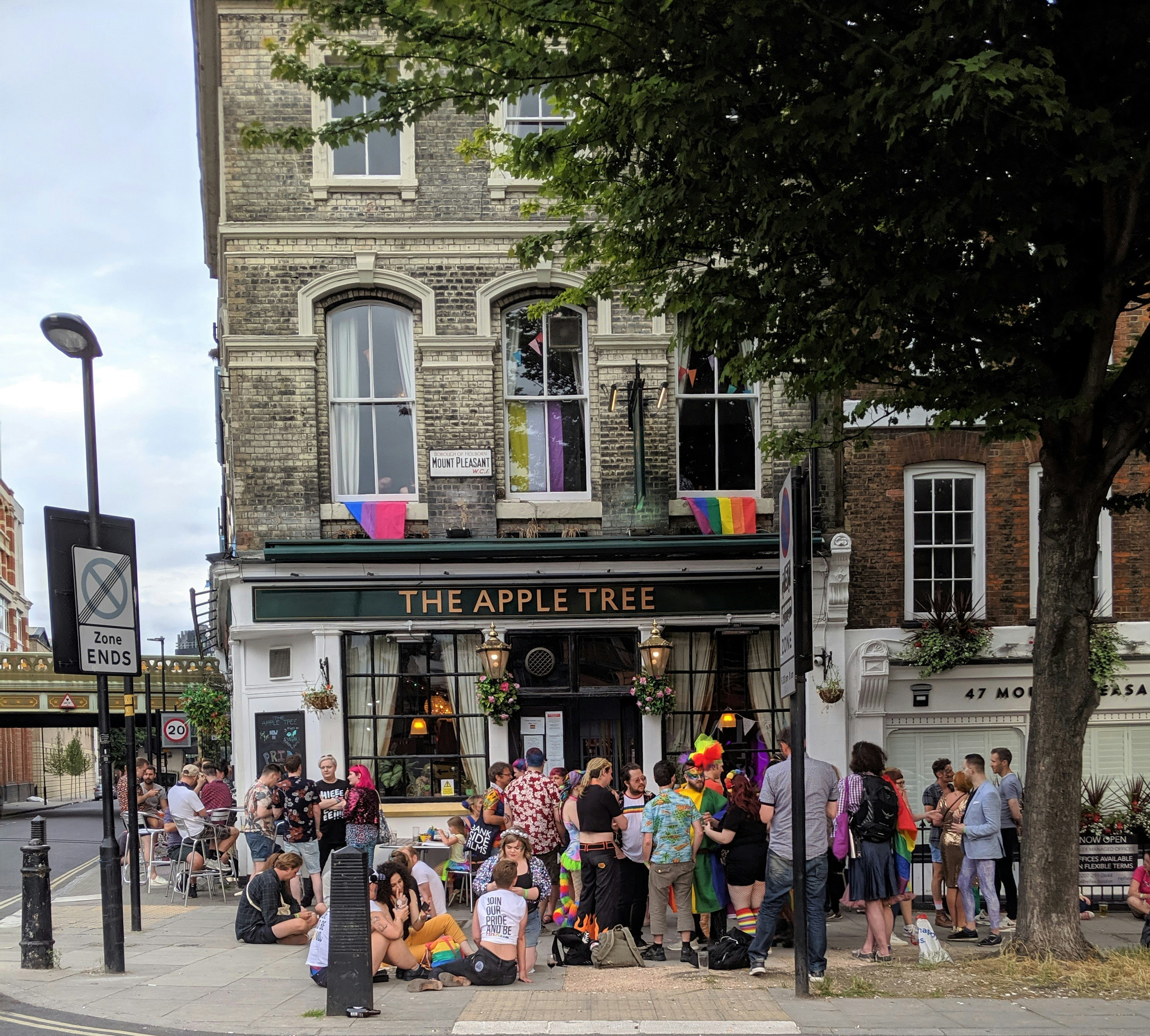 A group of people drinking and having fun outside a pub in a tall handsome Victorian building with a smart black sign saying the Apple Tree.