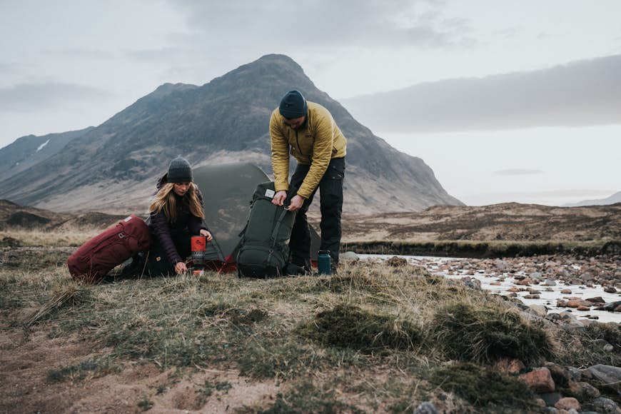 En man och kvinna packar upp utrustning från ryggsäckar i ett naturområde