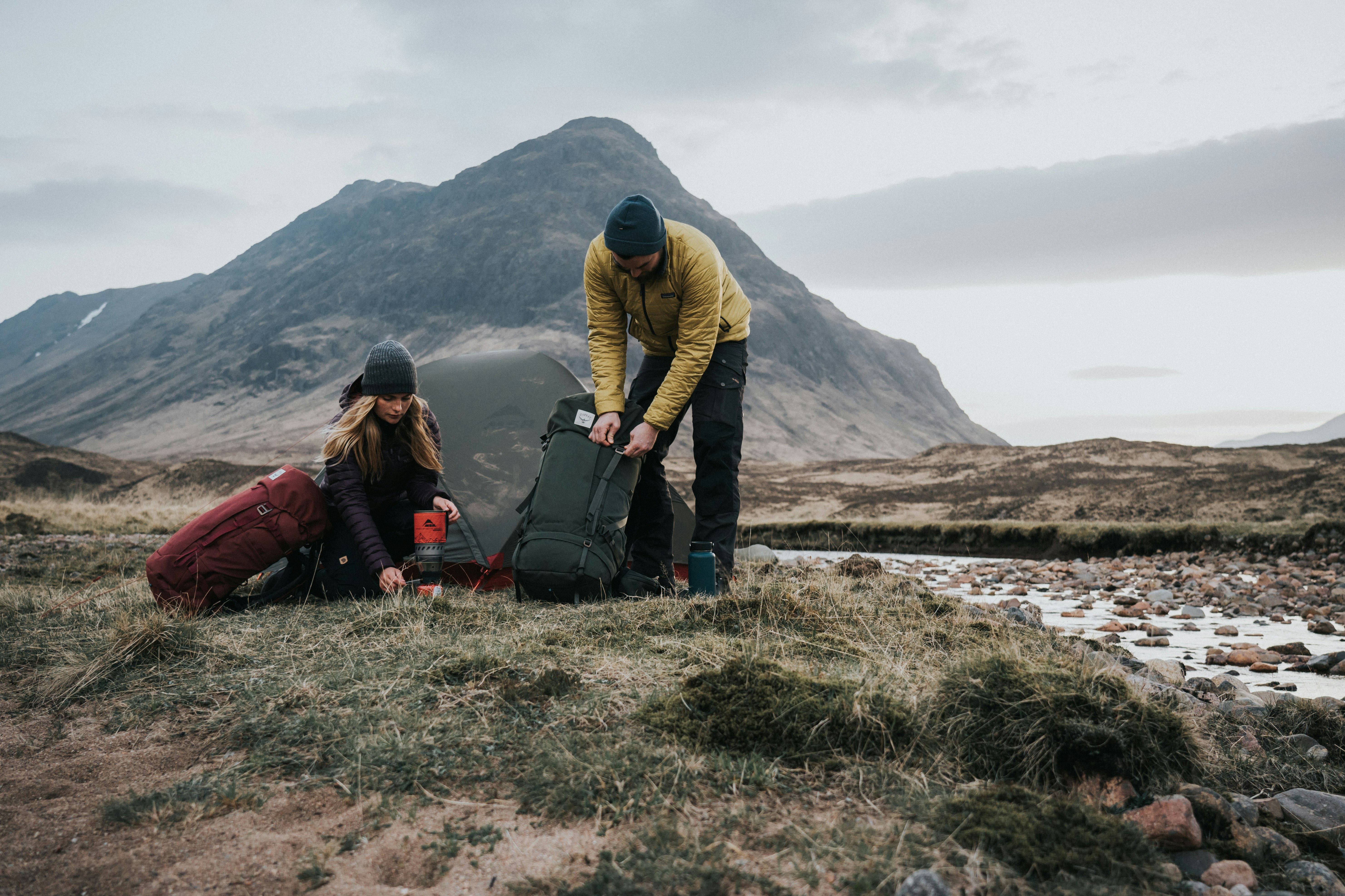 A man and woman unpack equipment from backpacks in a natural area