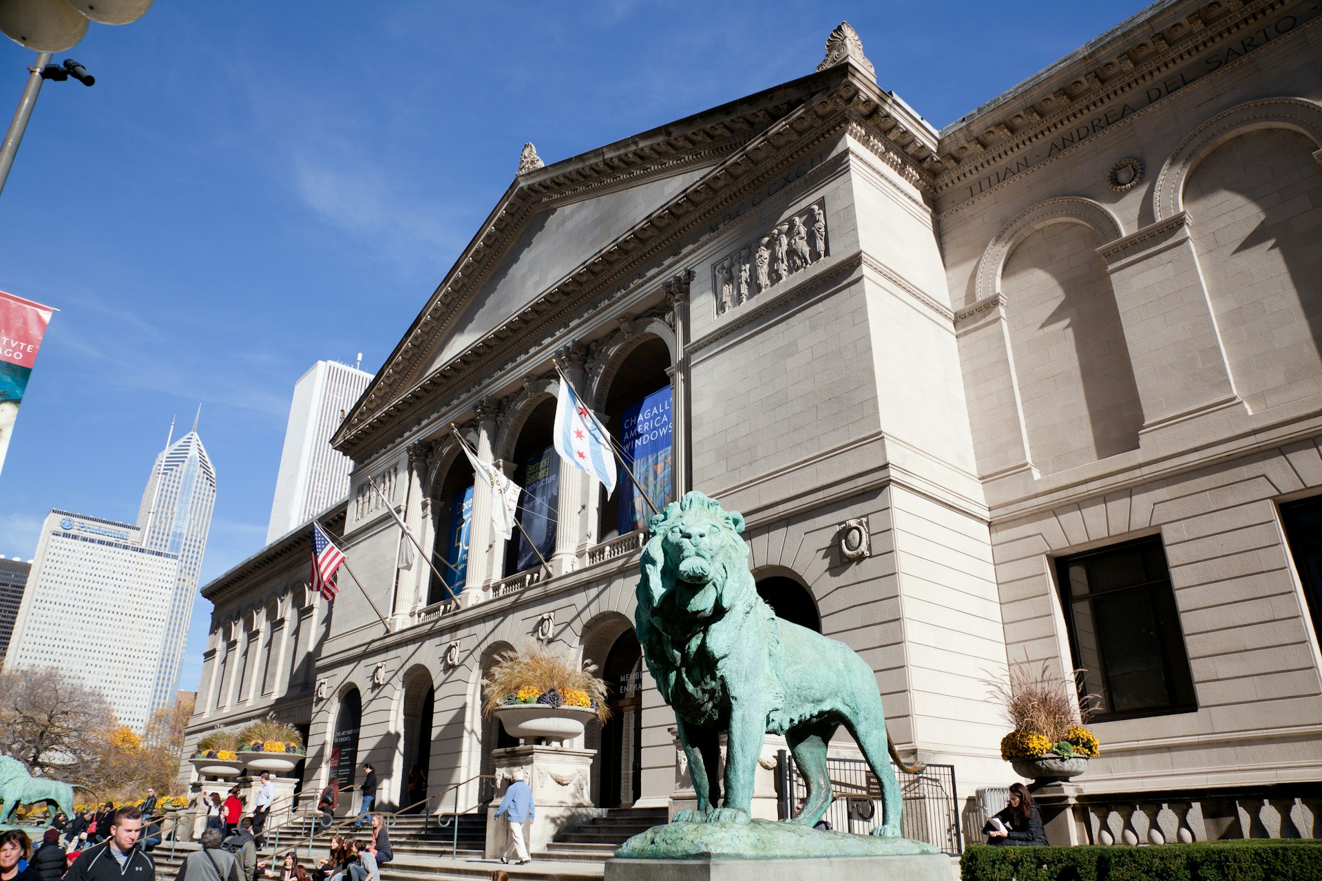 An oxidized lion statue stands in front of the Art Institute of Chicago building, whose facade rises in the background; perfect weekend in Chicago