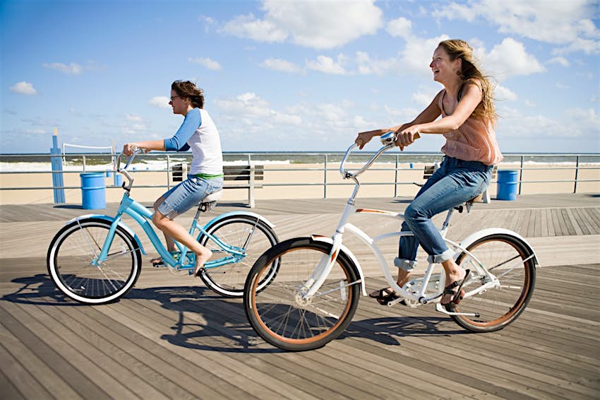 Two people ride bikes down a boardwalk 