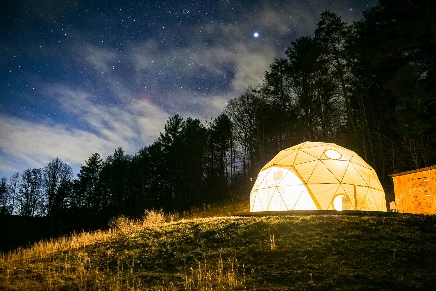 A geodesic lit from the inside, with dark trees and a night sky above