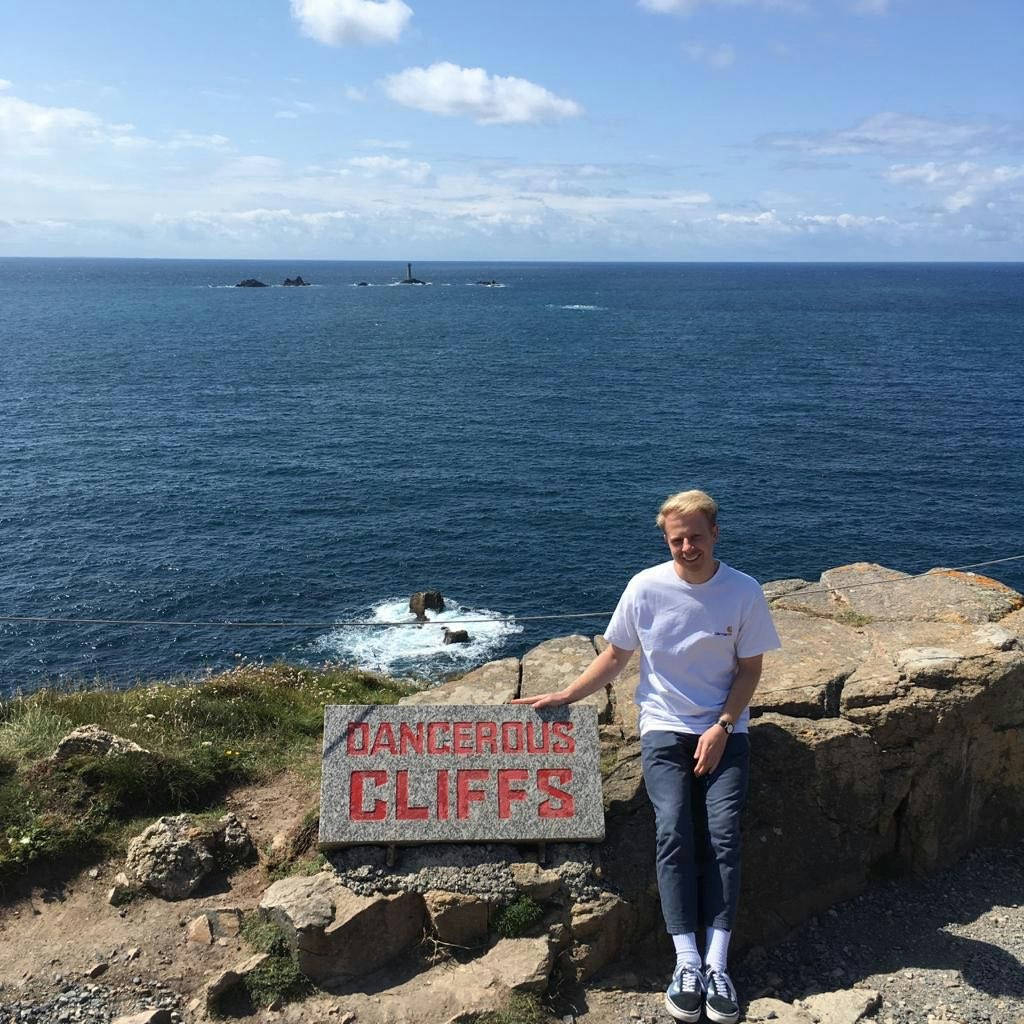 The author poses with a sign that reads 'Dangerous Cliffs' in red text.