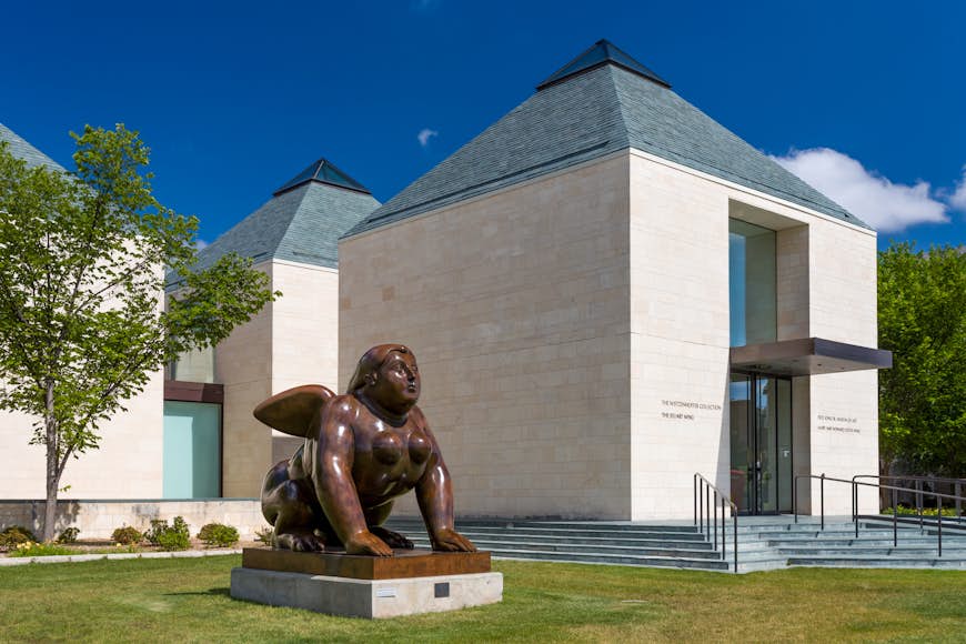 A giant sphinx sits outside a white-brick building with a teal roof; Norman vs Austin
