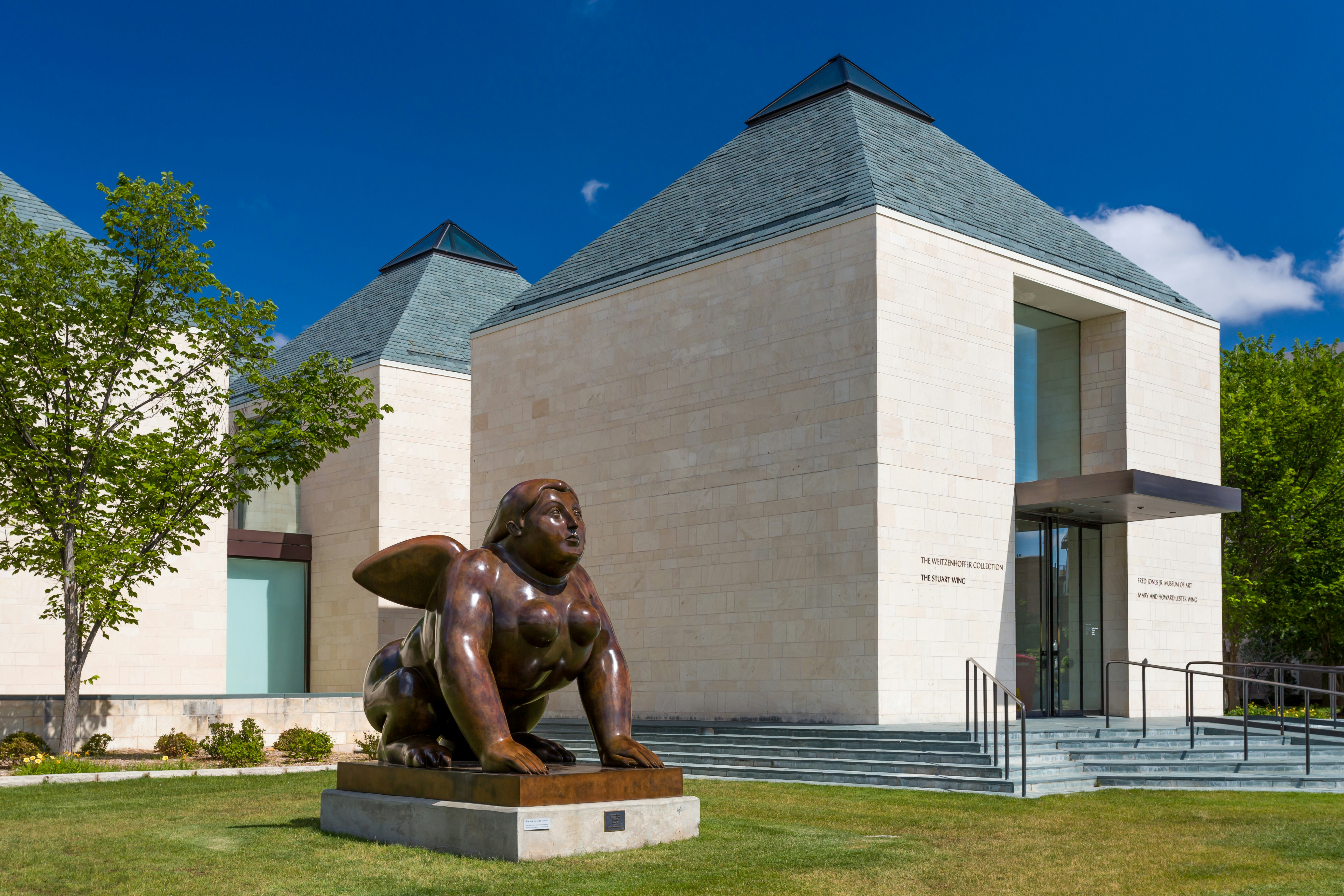 A giant sphinx sits outside a white-brick building with a teal roof; Norman vs Austin