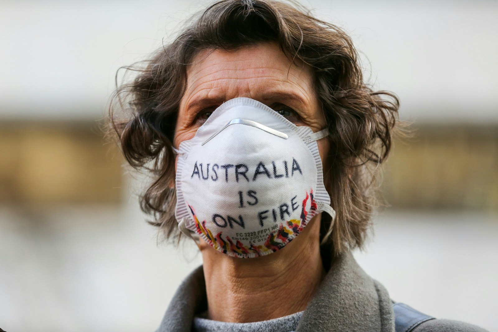 A woman wearing a white air pollution mask with 'Australia is on fire' written on it.