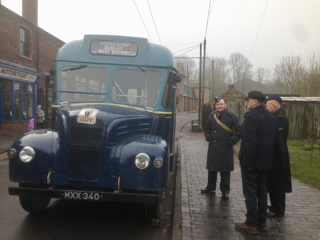 Three men in period garb stand by a blue vintage bus in Birmingham