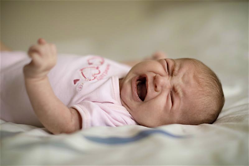 A newborn baby in a pink top crying while lying on a blanket