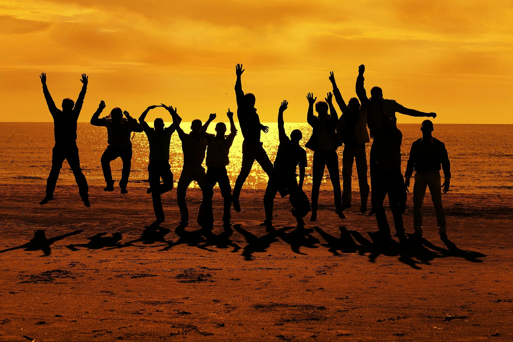 A group of bachelor party attendees silhouetted on a beach against a vivid yellow sunset, jumping up in the air.