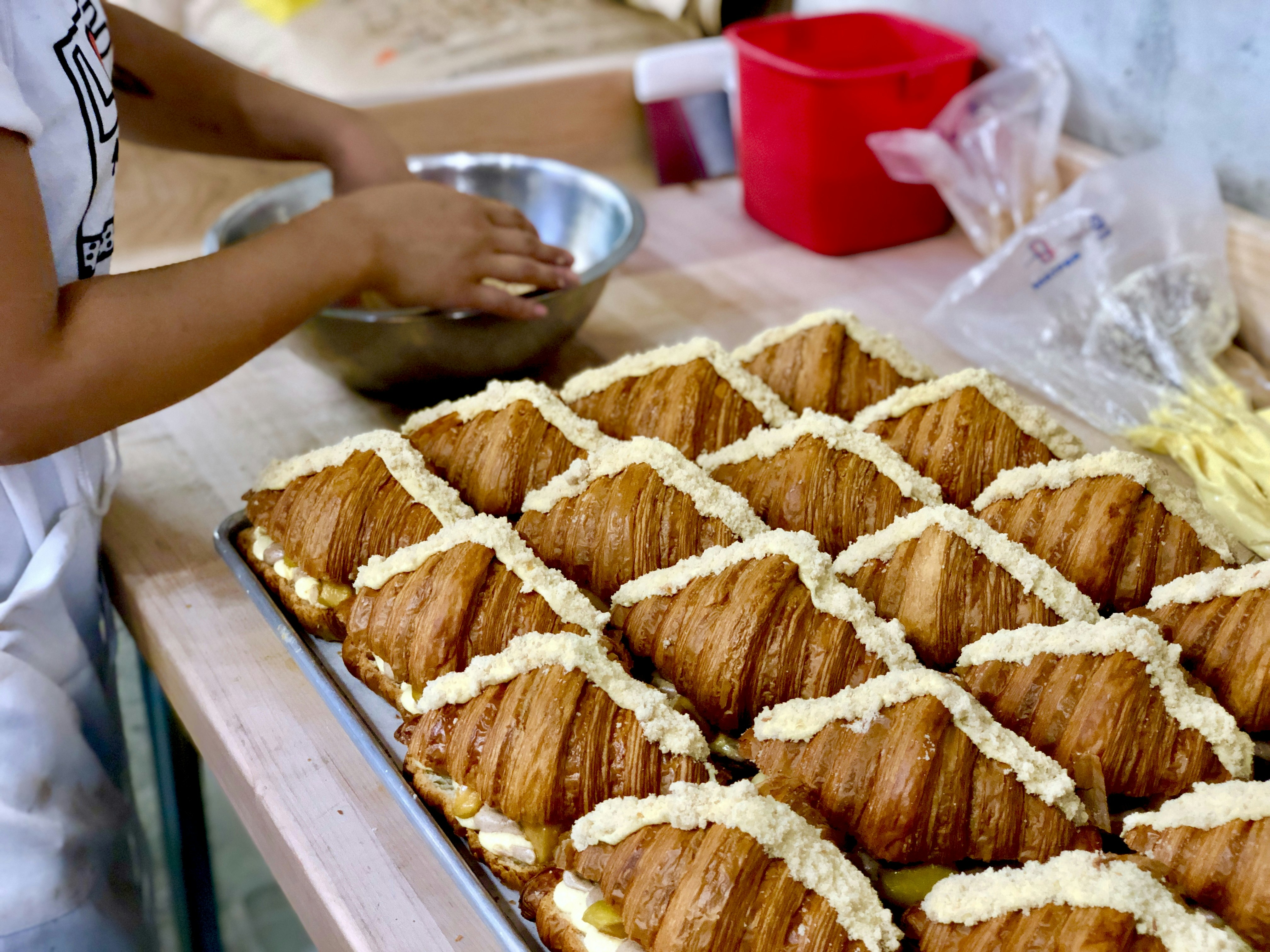 En bricka med croissanter bredvid en persons händer i en skål i köket i Supermoon Bakehouse, New York City