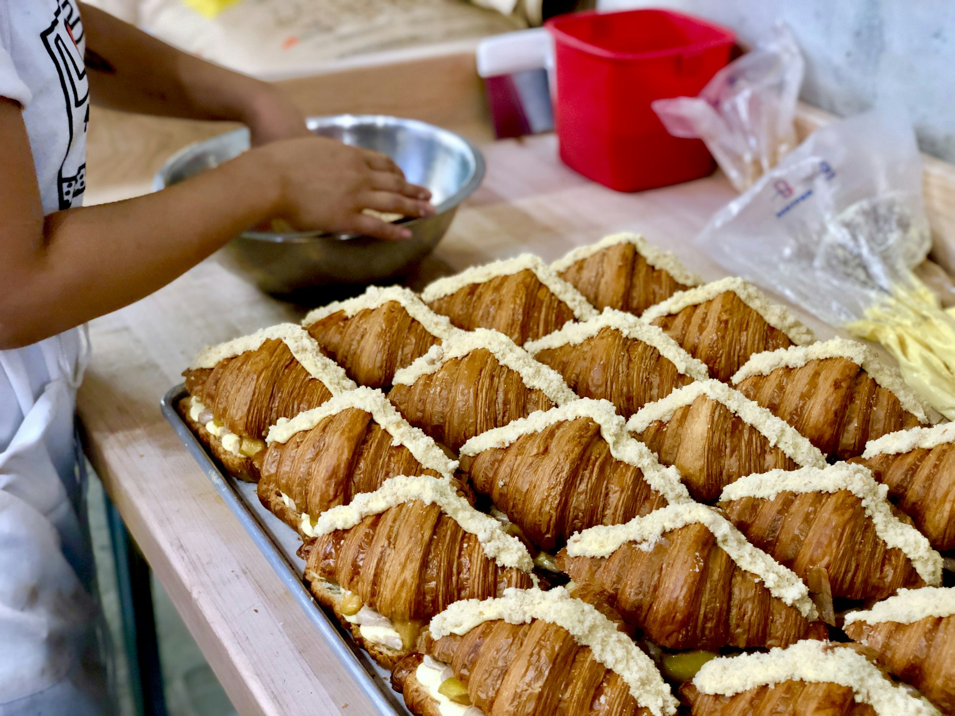 A tray of croissants beside a person's hands in a bowl in the kitchen of Supermoon Bakehouse, New York City