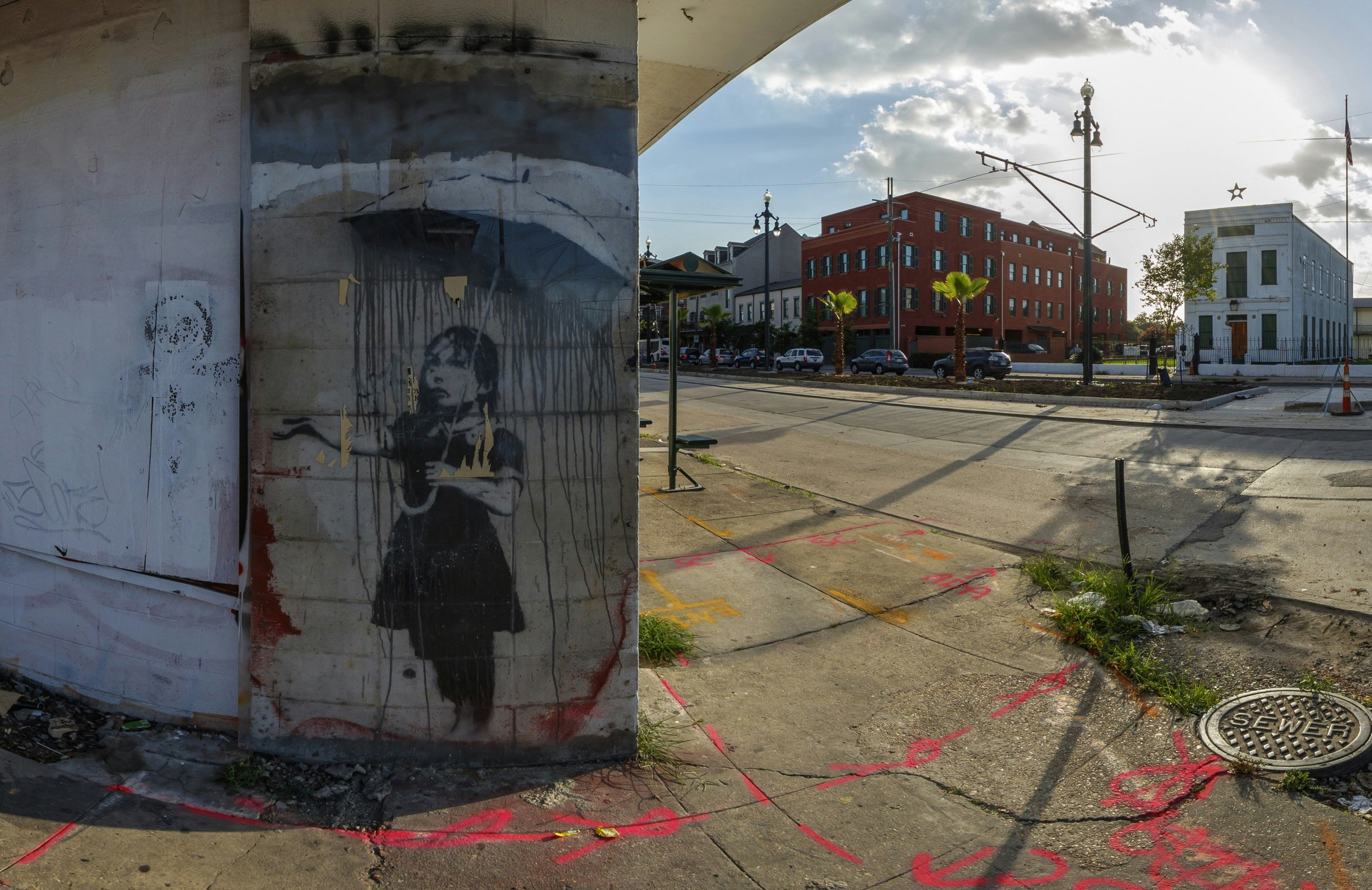 A painting of a girl reaching out from under an umbrella is painted on a building in New Orleans; Banksy in America