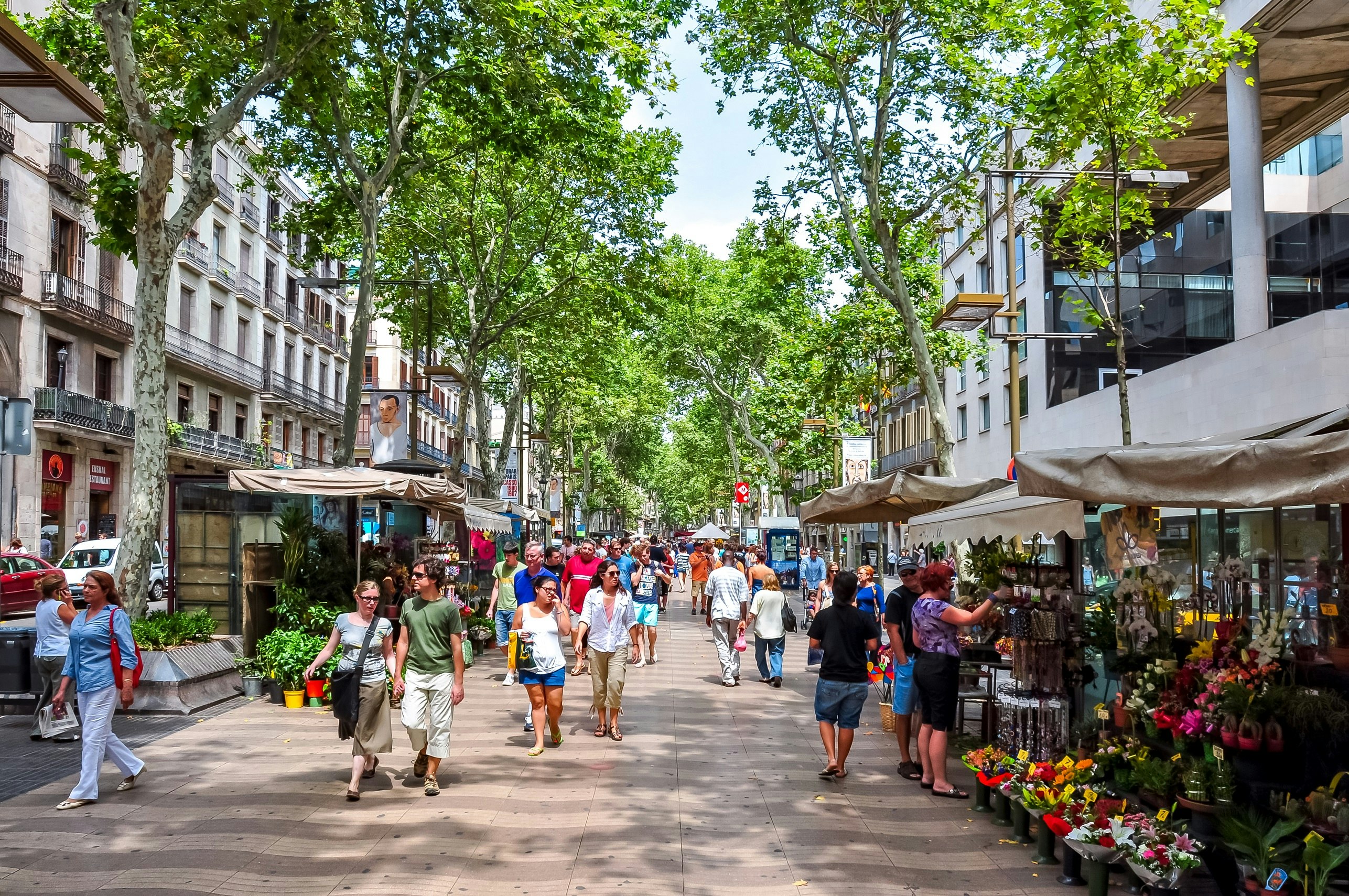 A pedestrianised street in the centre of Barcelona, with many people walking down it. Various stalls dot the edges.