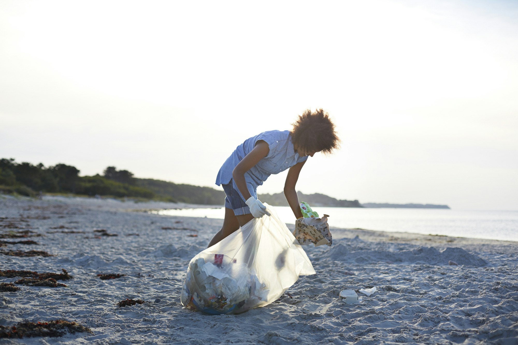 A woman cleans up litter and rubbish on a beach
