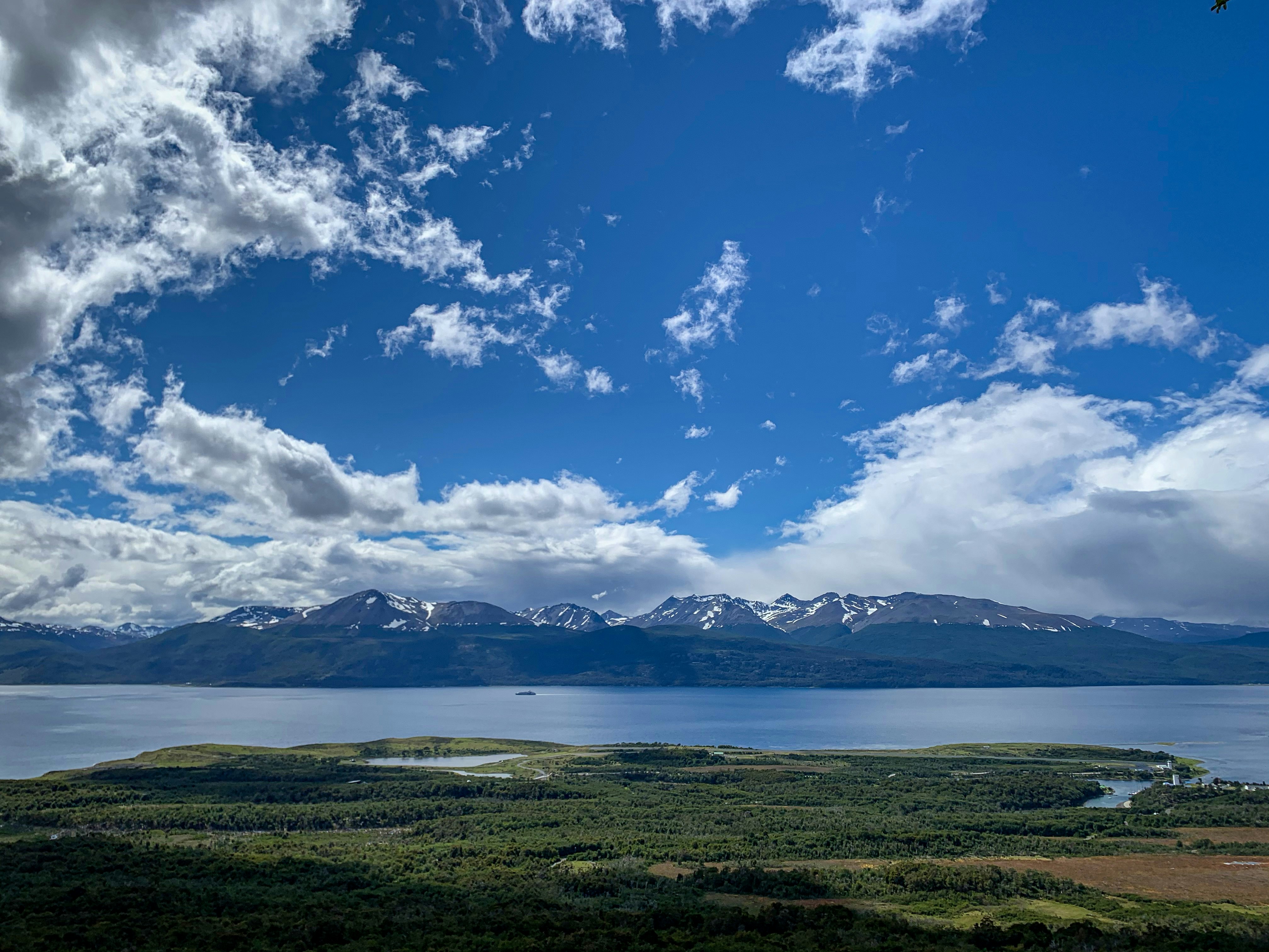 A flat, tree-covered piece of land is separated from a mountain range by a wide body of water, the Beagle Channel. 