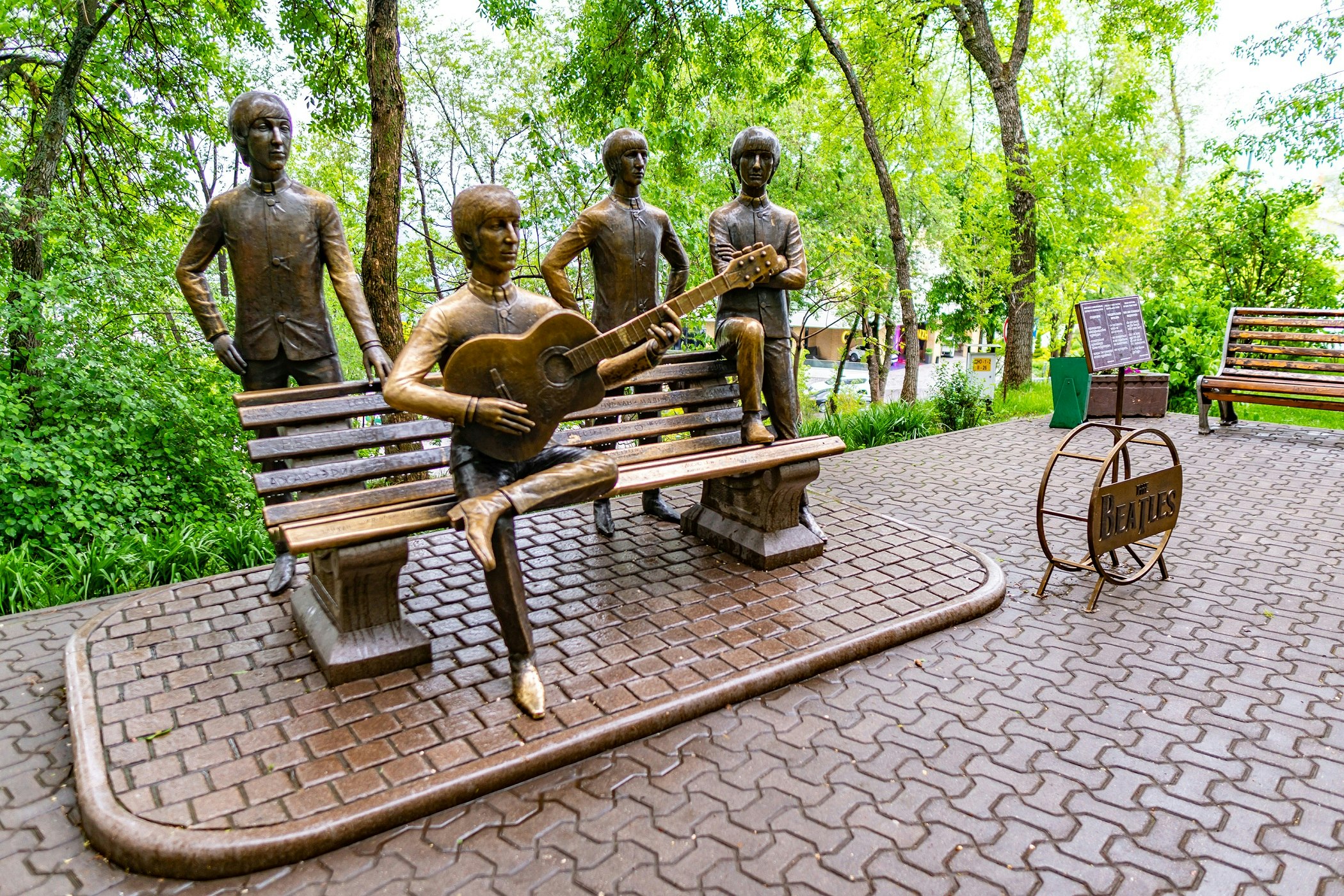 A bronze statue of British rock band The Beatles in Kok Tobe's hilltop amusement park. The four members of the band are life size, and sat on and stood around a bench.