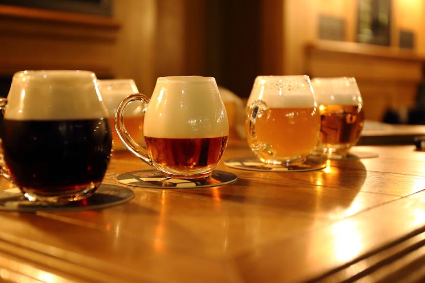 Fyra glas öl i olika färgnyanser ställs i rad på en träyta 