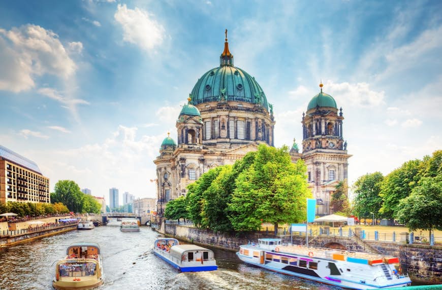 Passagerarbåtar driver nerför floden Spree en solig dag.  Berliner Dom (Berlin-katedralen) är synlig. 
