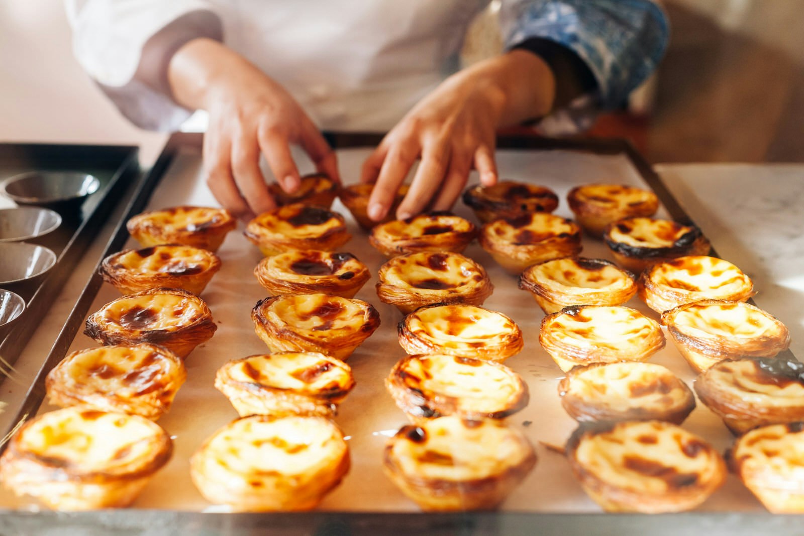 A baker arranging pasteis de nata on a tray in Lisbon.