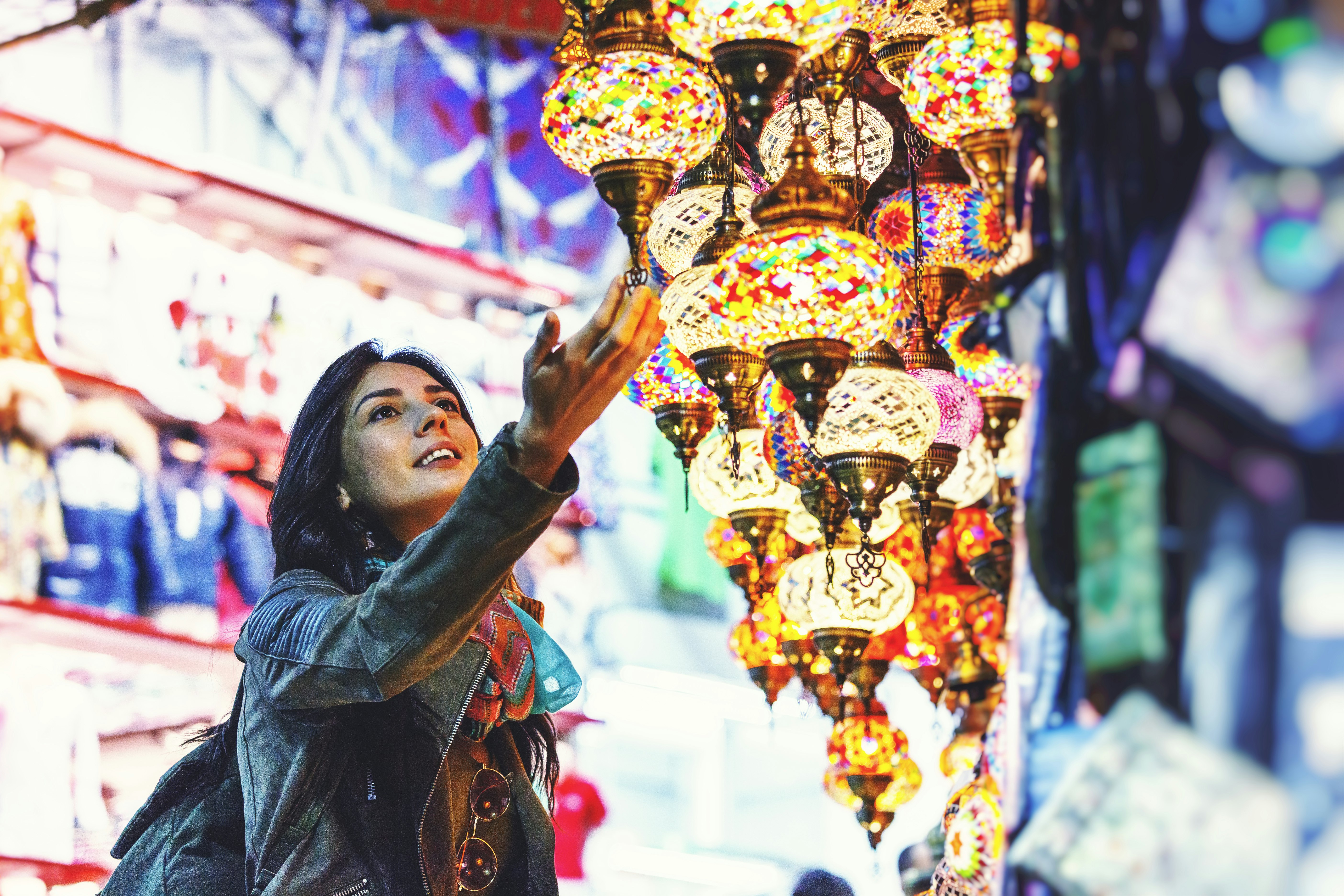 A woman lightly touches a multi-colored and ornate lantern hanging from a shop stall 