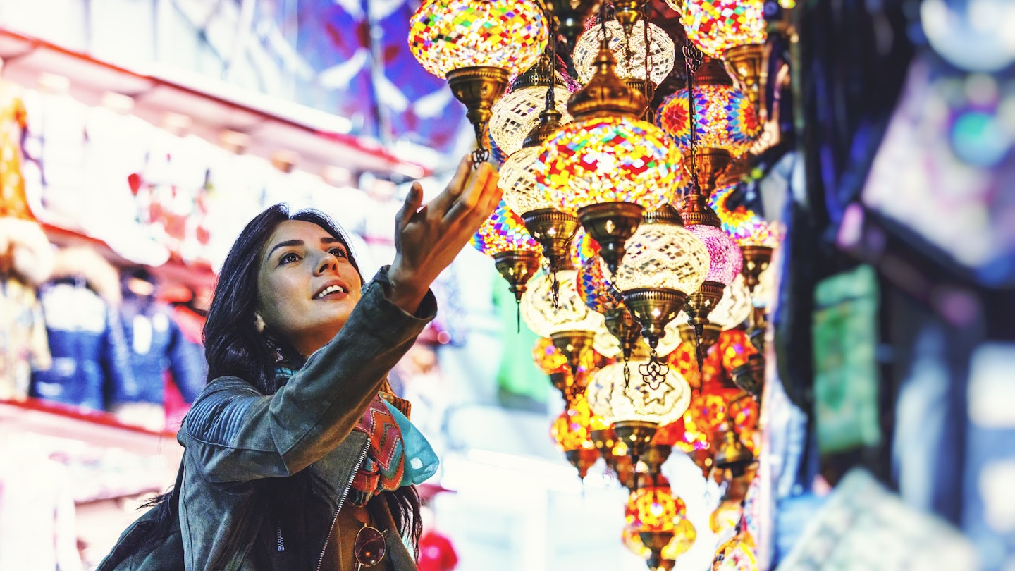 A woman lightly touches a multi-colored and ornate lantern hanging from a shop stall 
