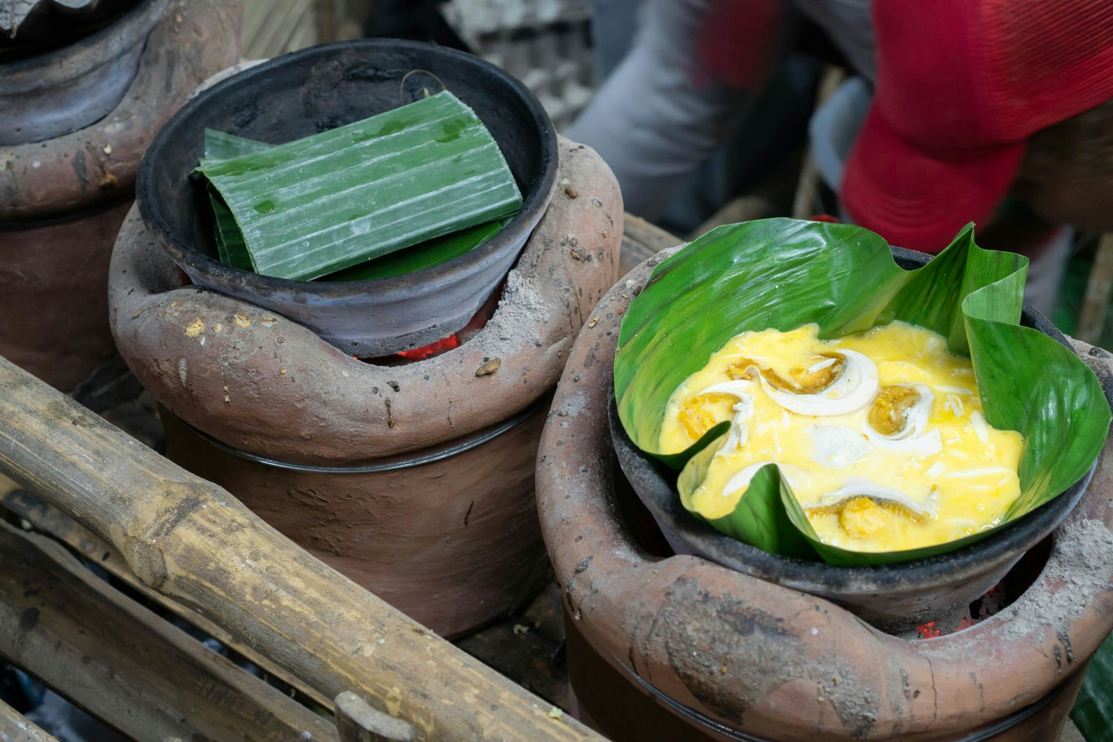 Bibingka being prepared in terracotta pots over hot coals, wrapped in banana leaves