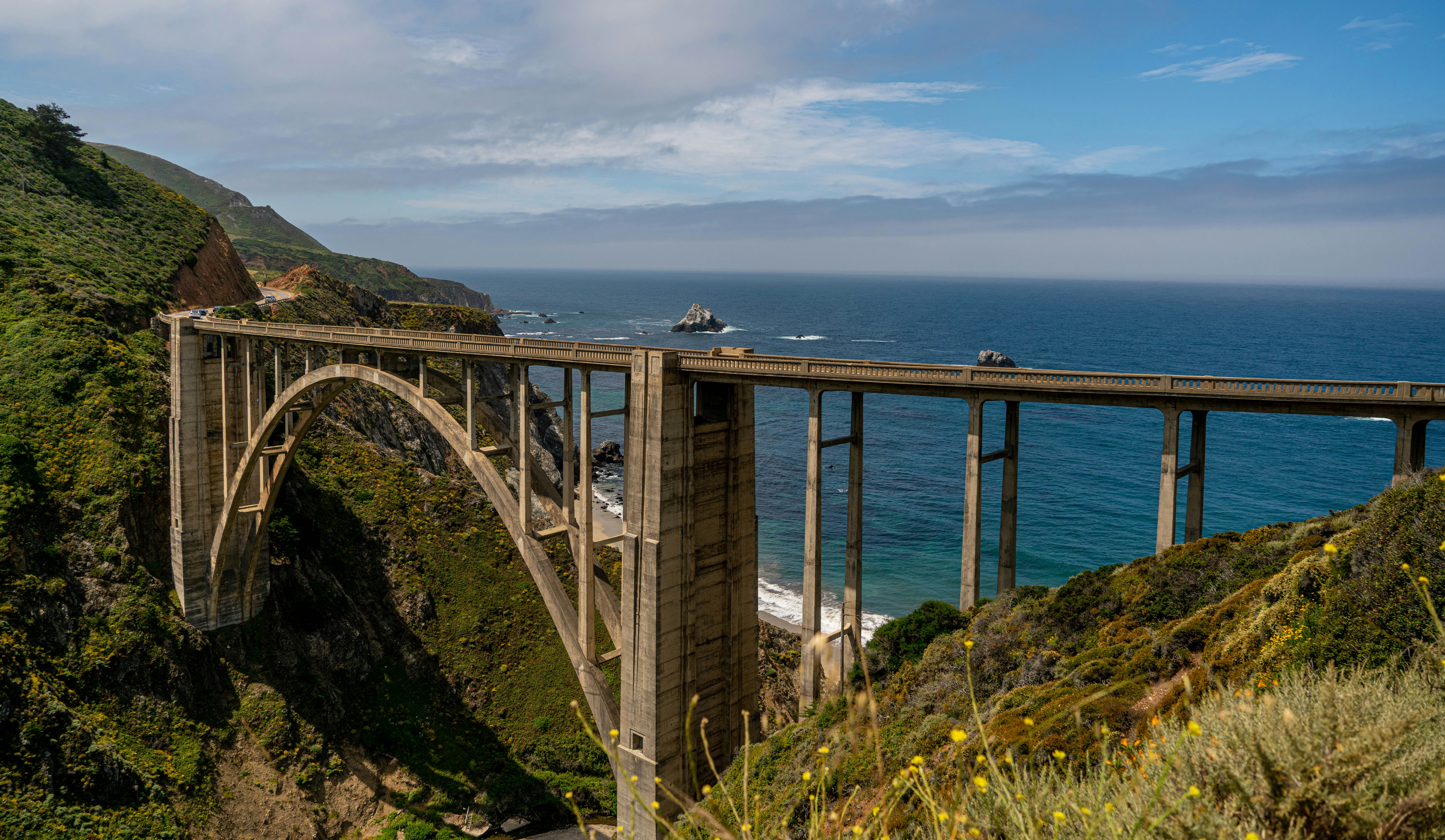 A massive single-span bridge made of concrete curves around a small ravine on the coast of California near Big Sur; California ice cream