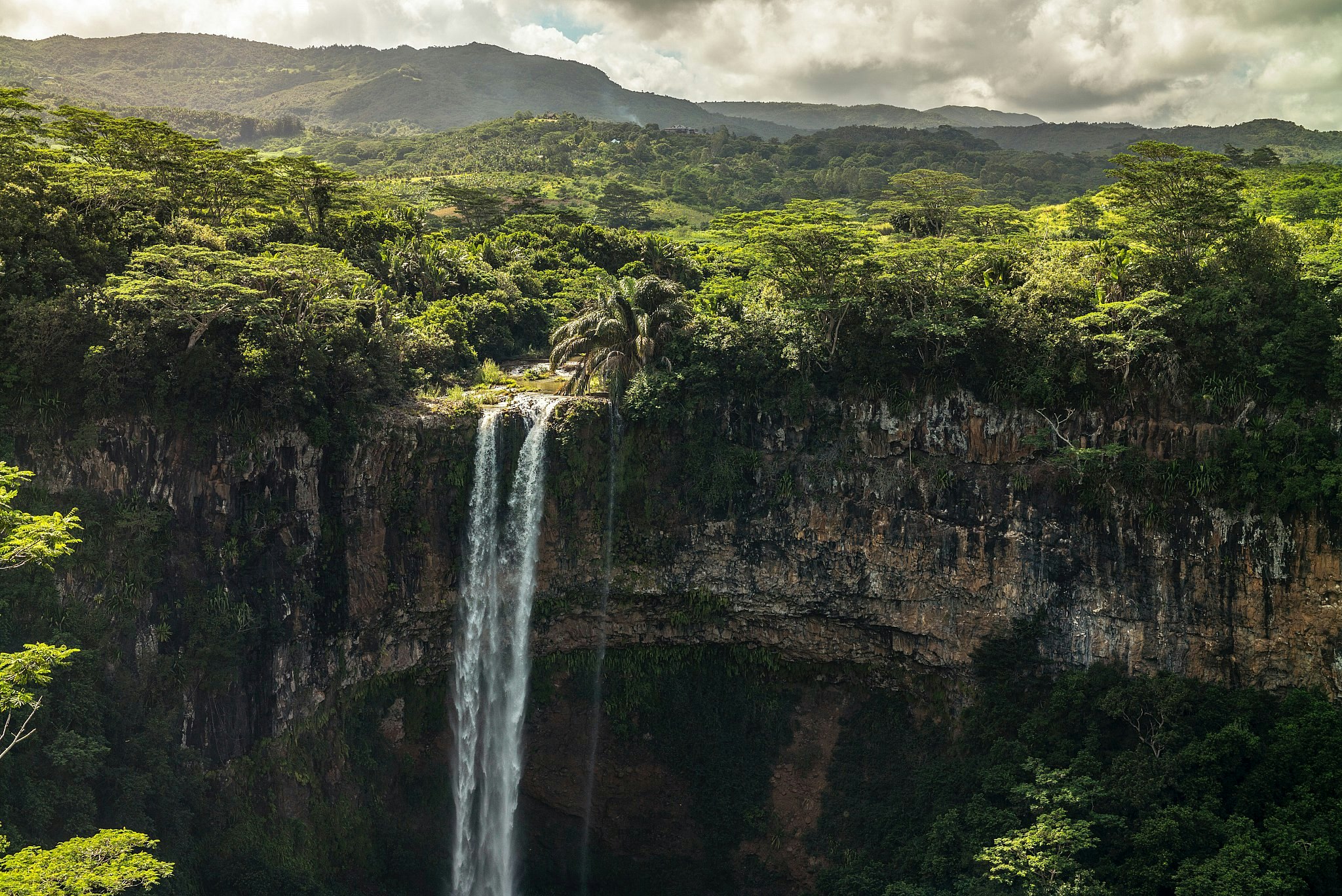 A waterfall cascades over a cliff face in front of verdant forest near Chamarel, Mauritius.