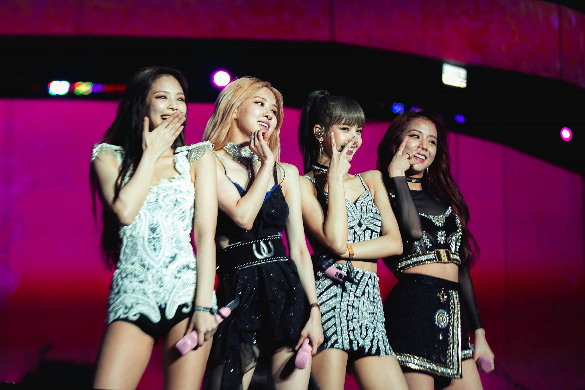 The four members of K-Pop girl group Blackpink pose on a pink-lit stage.