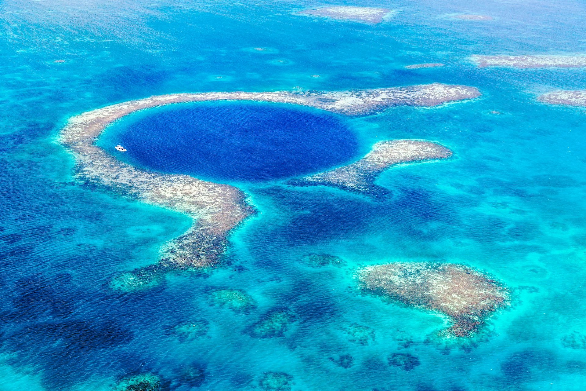 Aerial view over Belize's Great Blue Hole, a giant blue marine sinkhole encircled by an atoll, surrounded by paler turquoise waters.